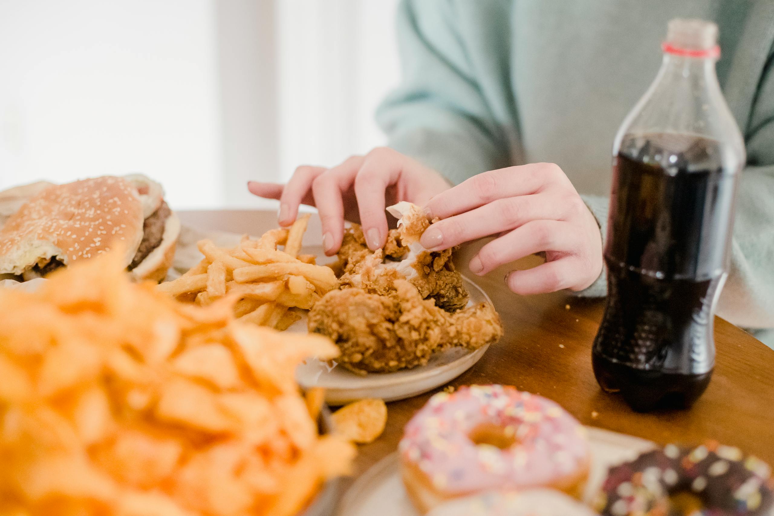 Crop anonymous female eating appetizing spicy fried chicked at table with different snacks