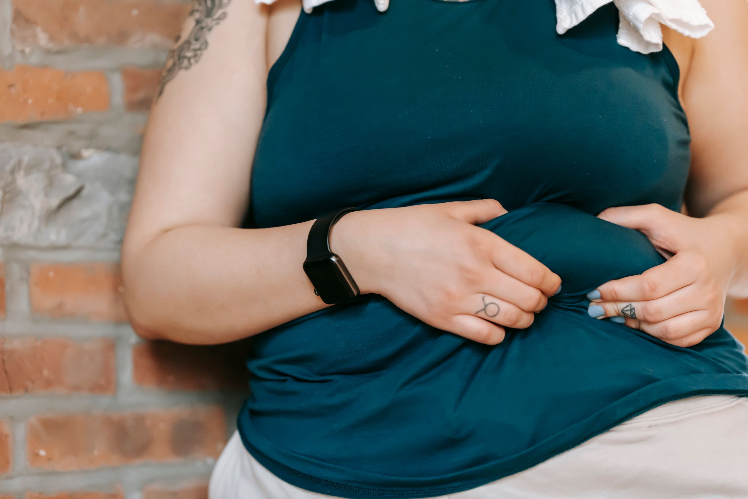 Crop anonymous plus size female demonstrating and touching belly while leaning on brick wall