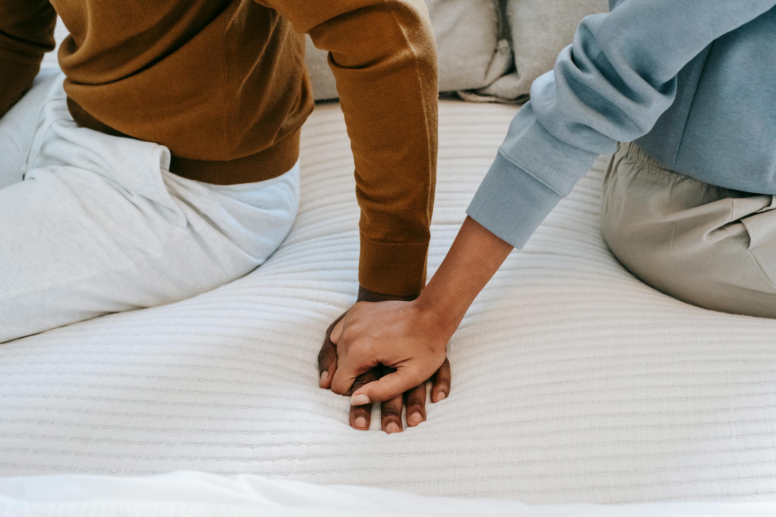Crop faceless African American couple sitting on bed back to back and holding hands