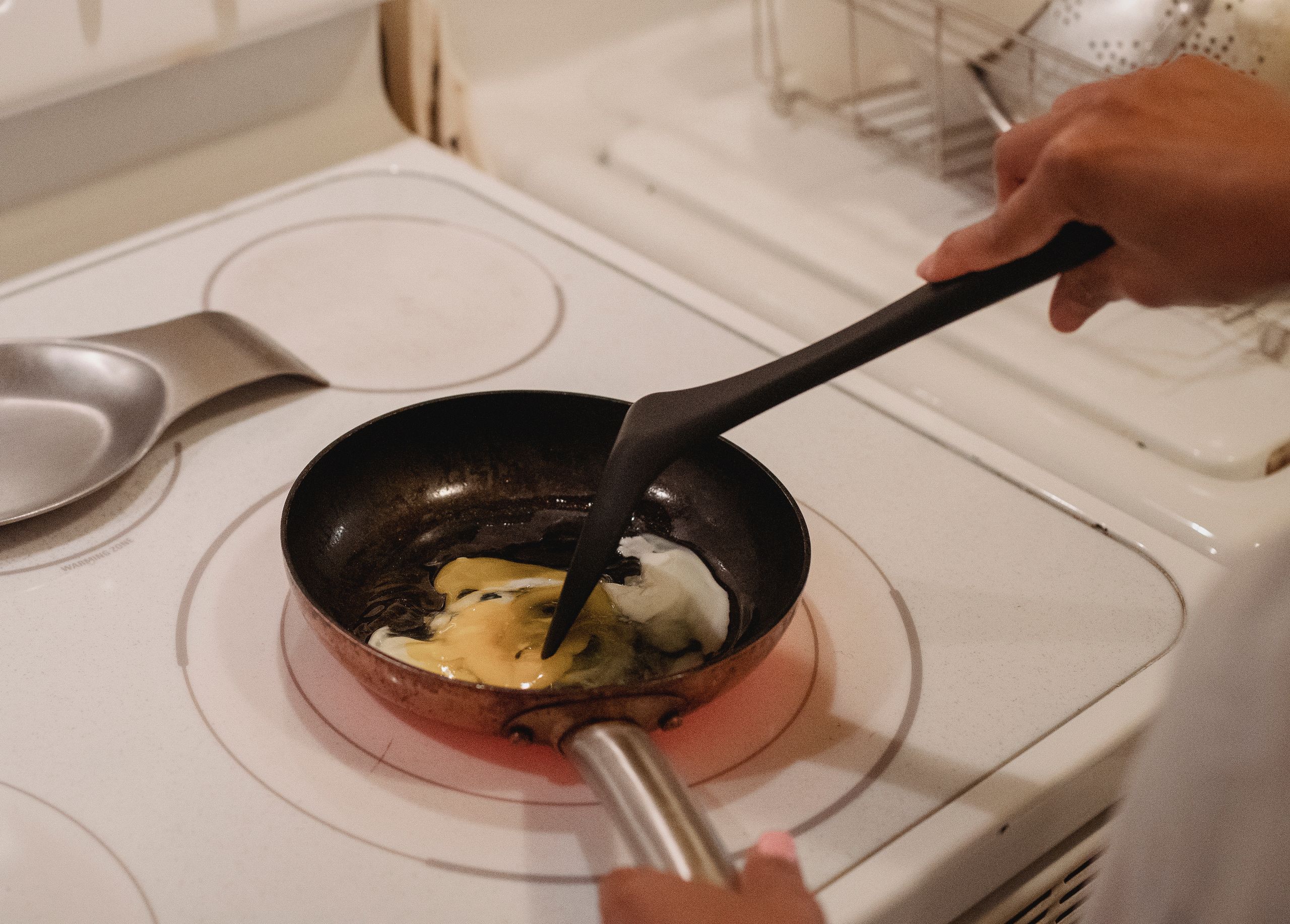 Crop unrecognizable person near white stove with black spatula cooking scrambled eggs in kitchen