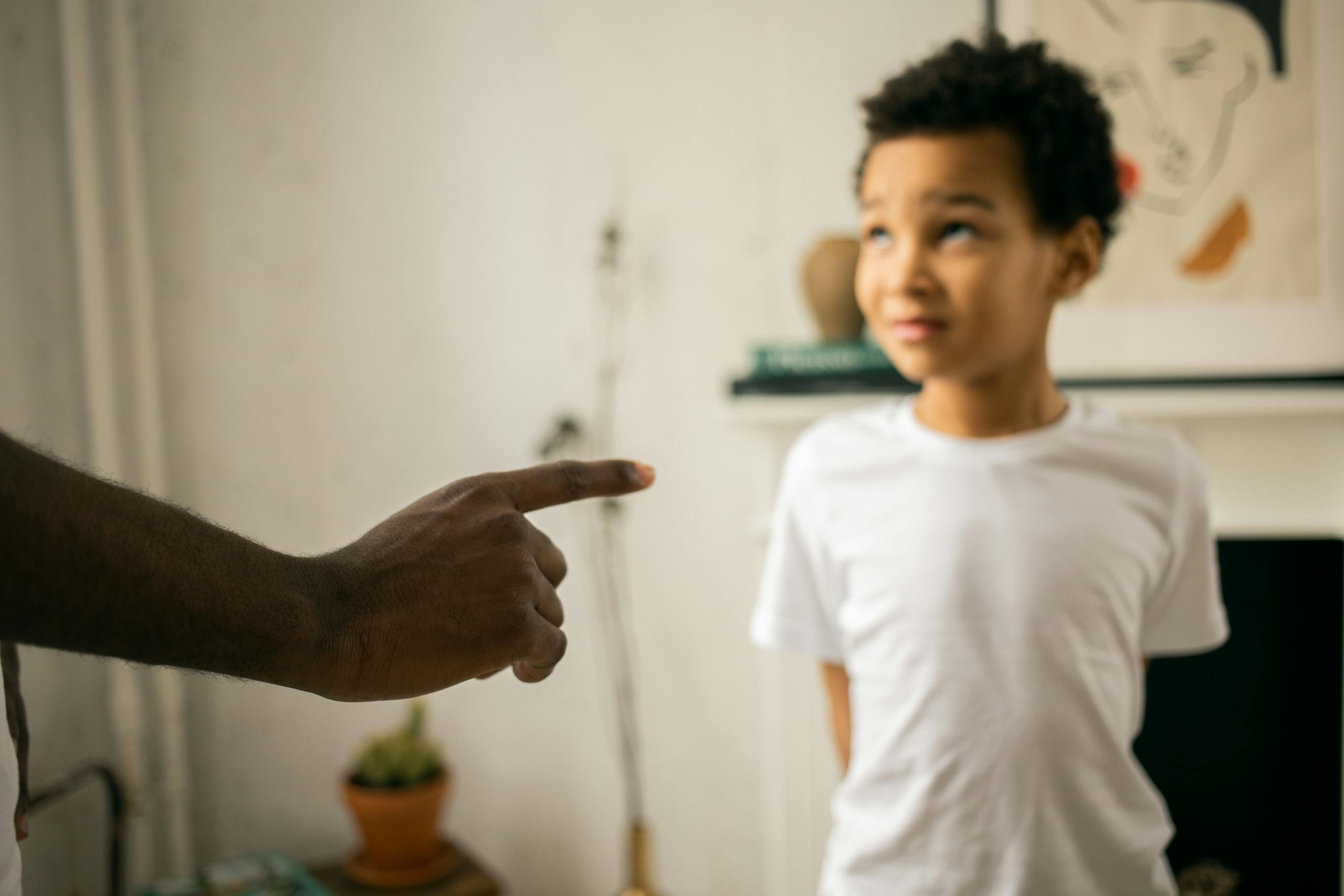 Crop unrecognizable strict black man scolding and disciplining guilty attentive little son standing with hands behind back and looking up