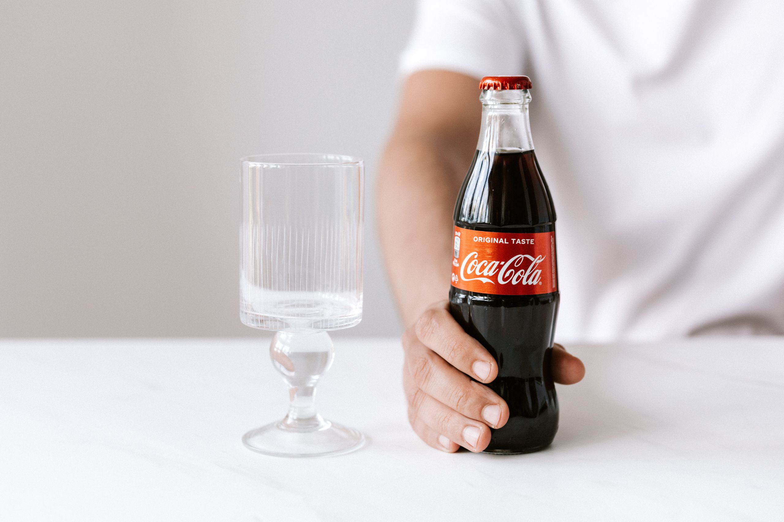 Crop unrecognizable young guy in white t shirt demonstrating bottle of cold coke