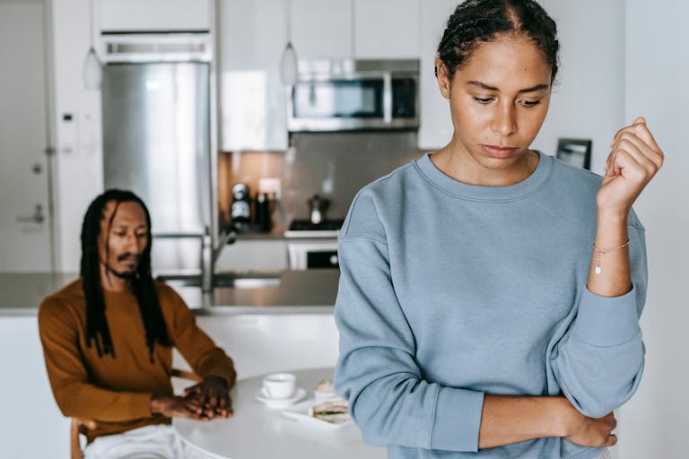 Crop upset African American female with pensive male partner at table during conflict in house