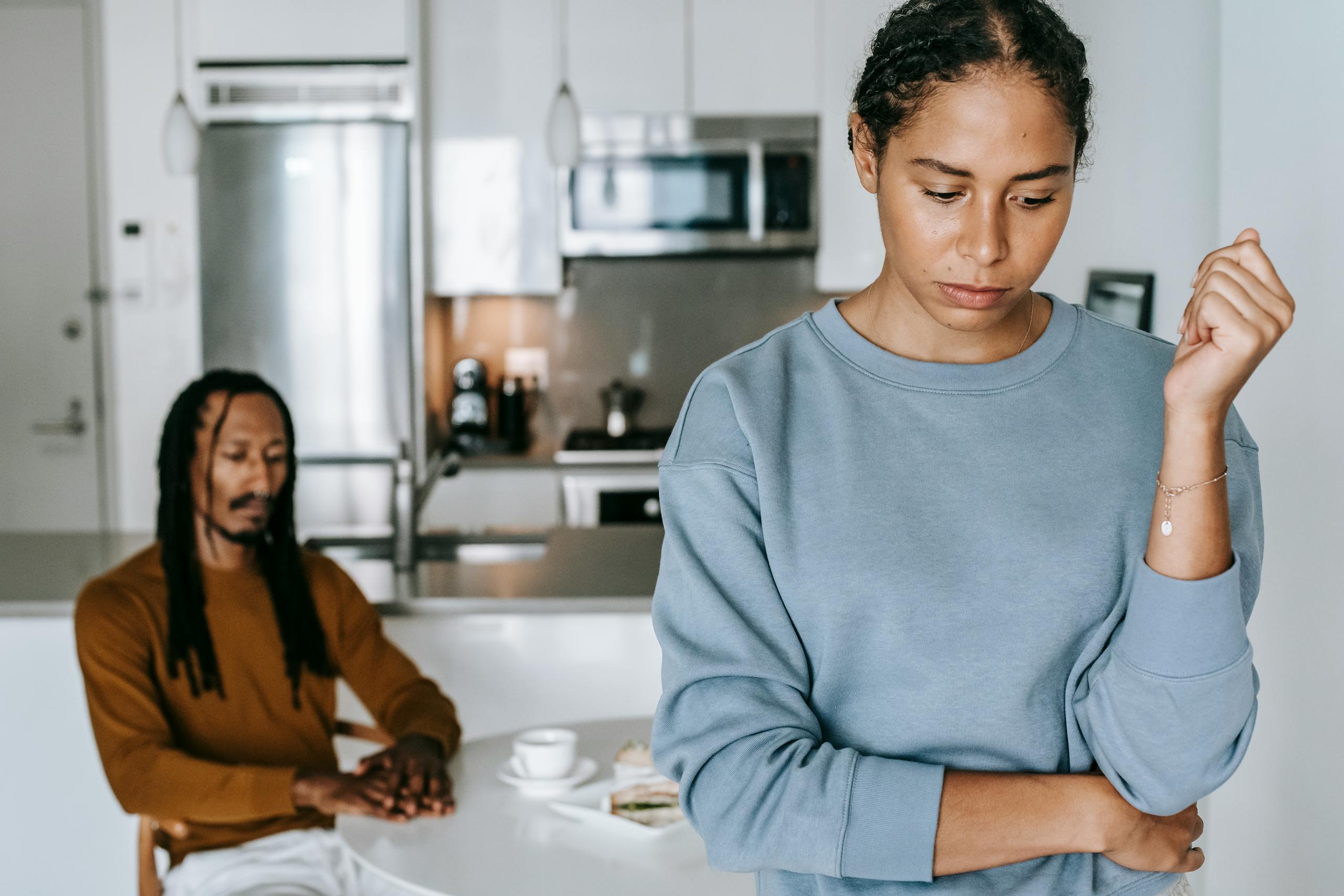 Crop upset African American female with pensive male partner at table during conflict in house