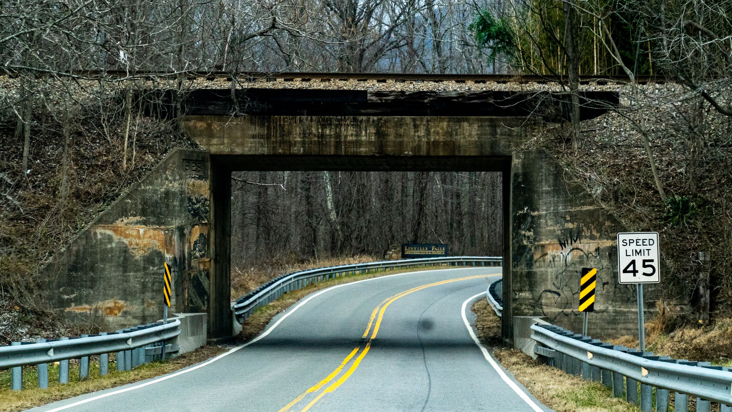 Curving road under an old railroad overpass surrounded by winter trees in Trade, TN.