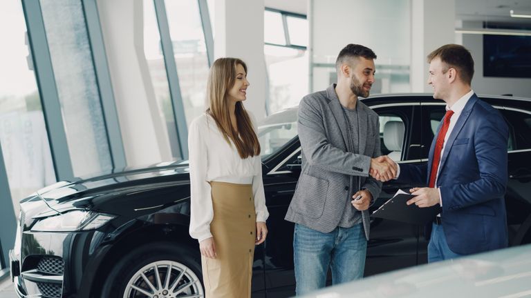 Customers shaking hands with dealer in showroom, sealing car purchase deal.