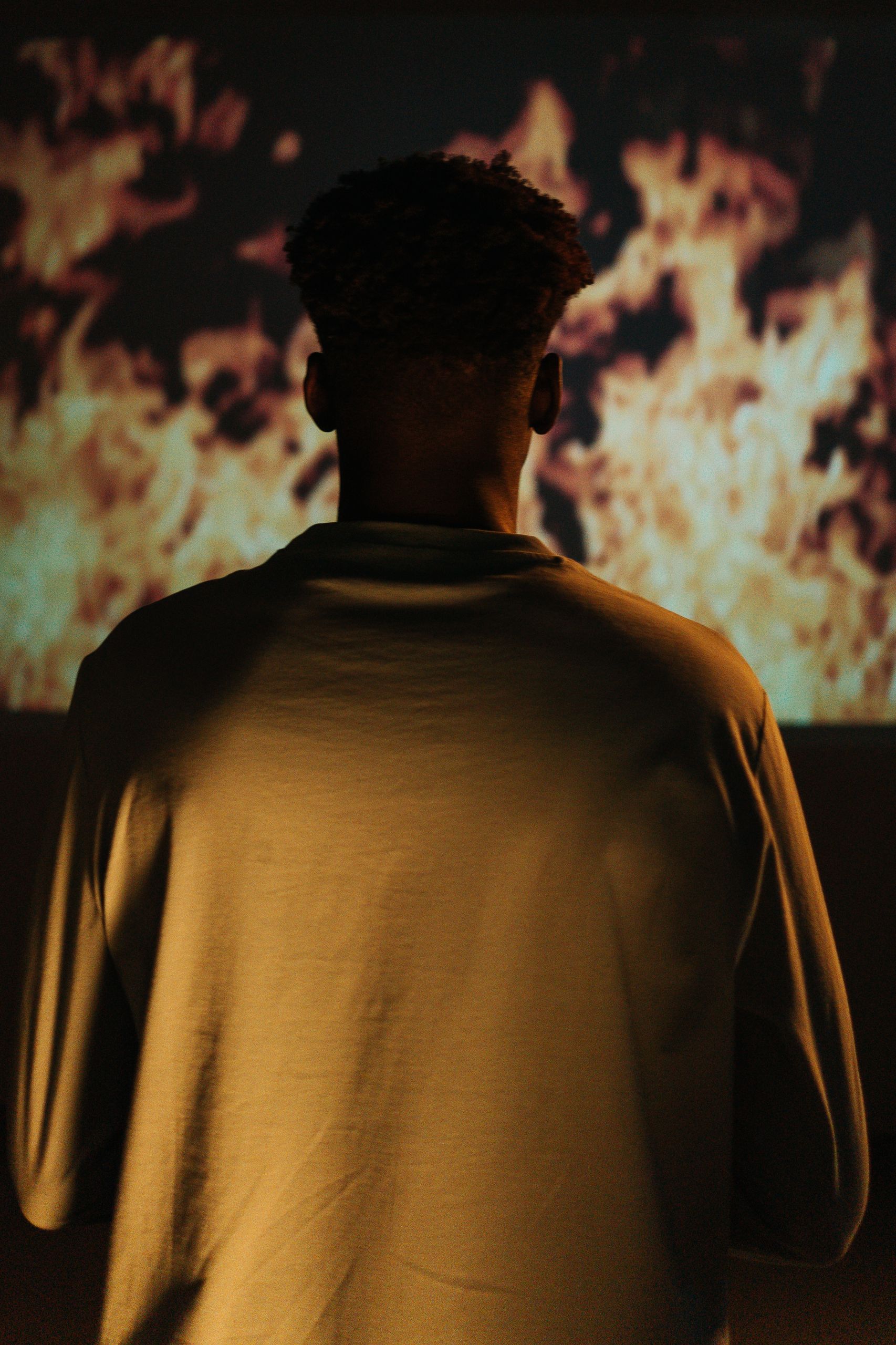 Dark silhouette of a man watching a fiery background indoors, creating a moody atmosphere.