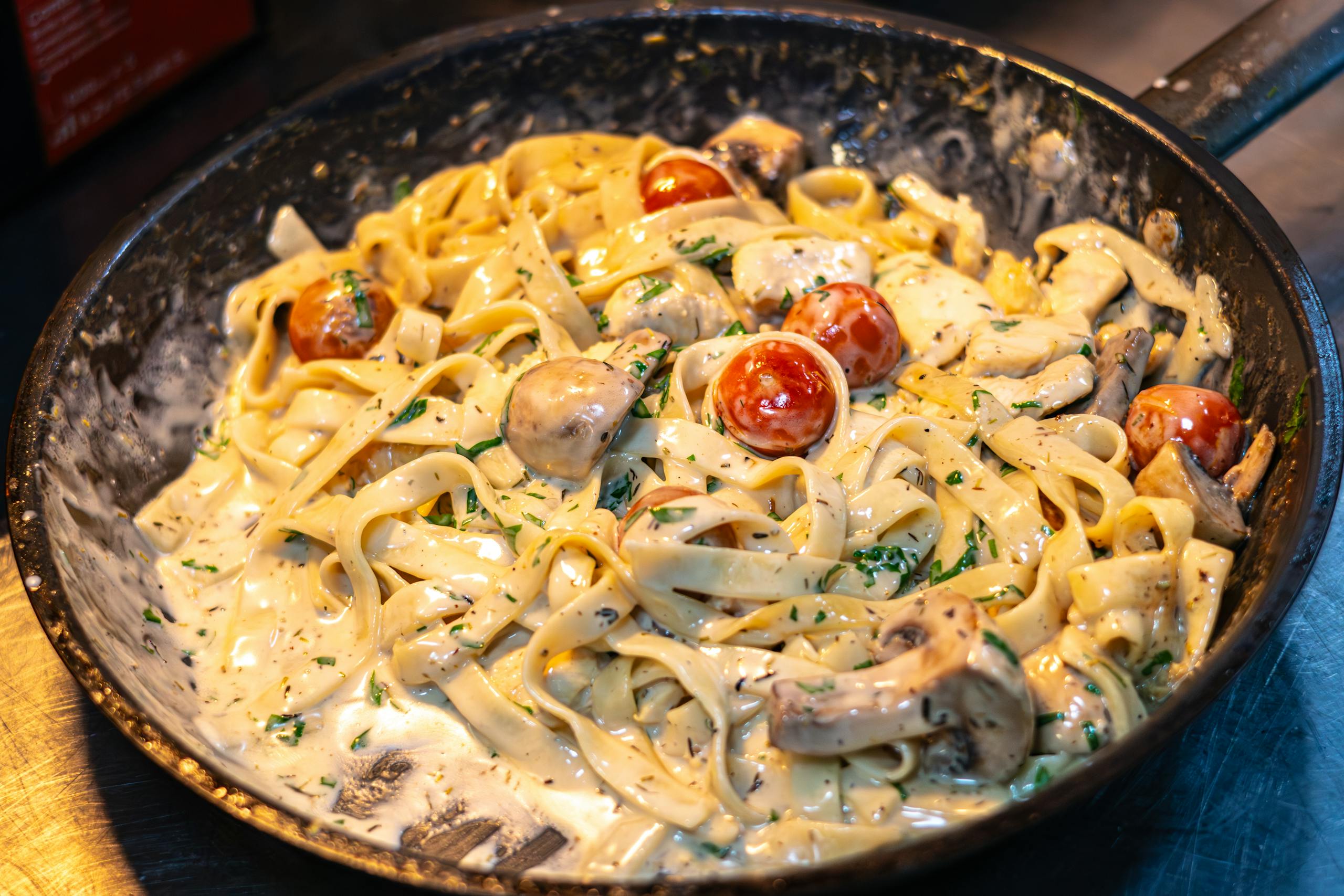 Delicious creamy fettuccine pasta with mushrooms and tomatoes in a skillet, perfect for Italian cuisine lovers.