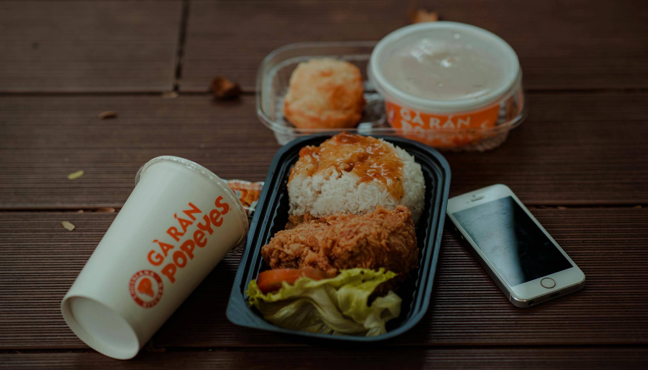 Delicious fried chicken meal from Popeyes with accompanying smartphone and drink on wooden table.