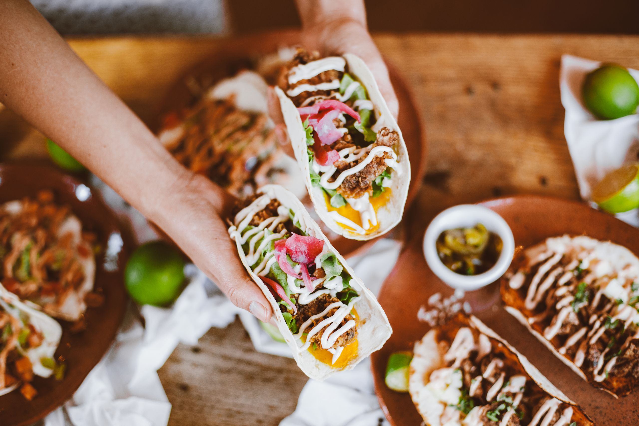 Delicious handheld tacos with fresh toppings and lime on a wooden table.