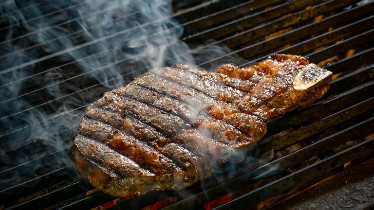 Delicious ribeye steak grilling on a barbecue with visible smoke and grill marks.