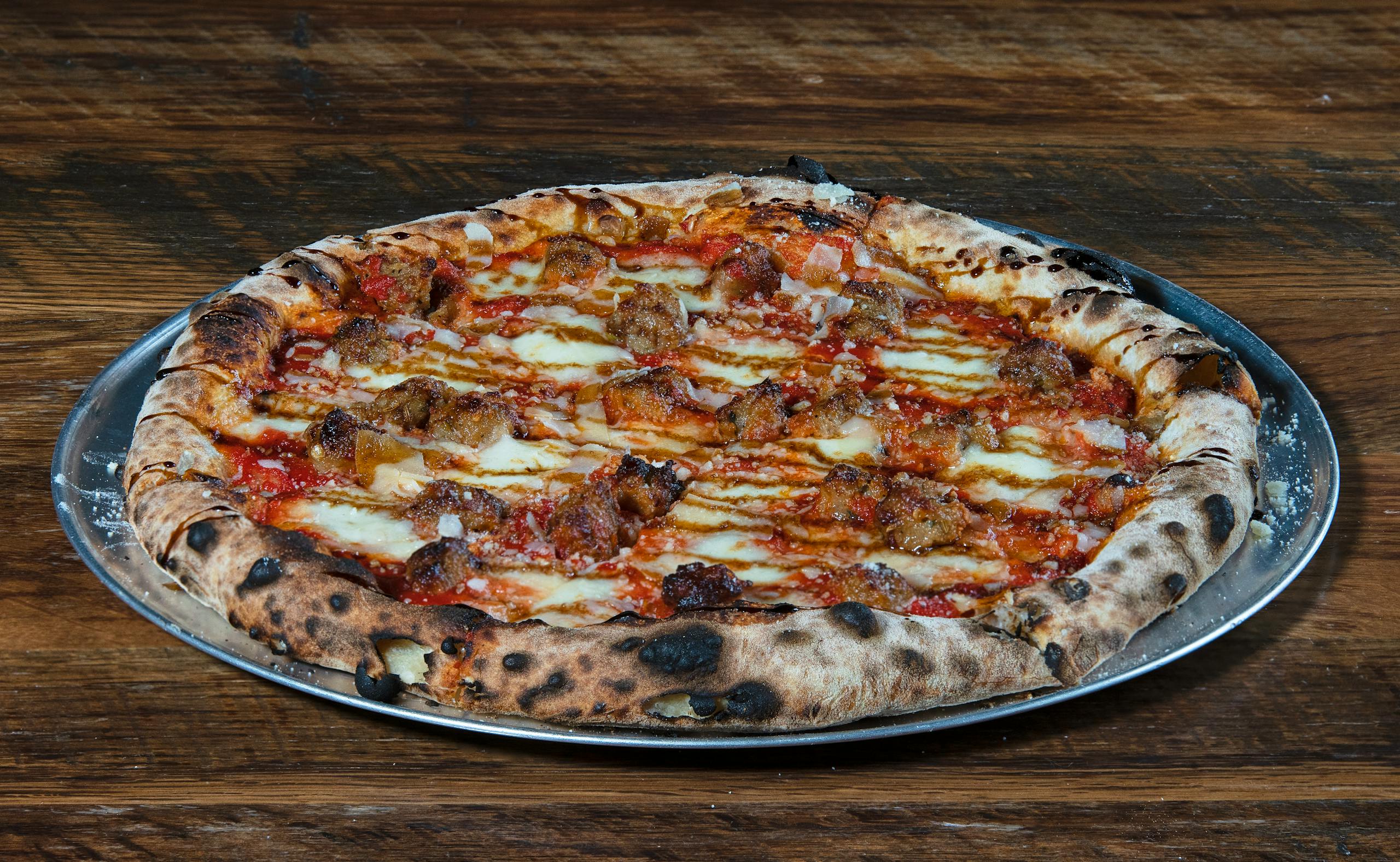 Delicious wood-fired pizza with Italian sausage on a metal tray. Perfect for food lovers.