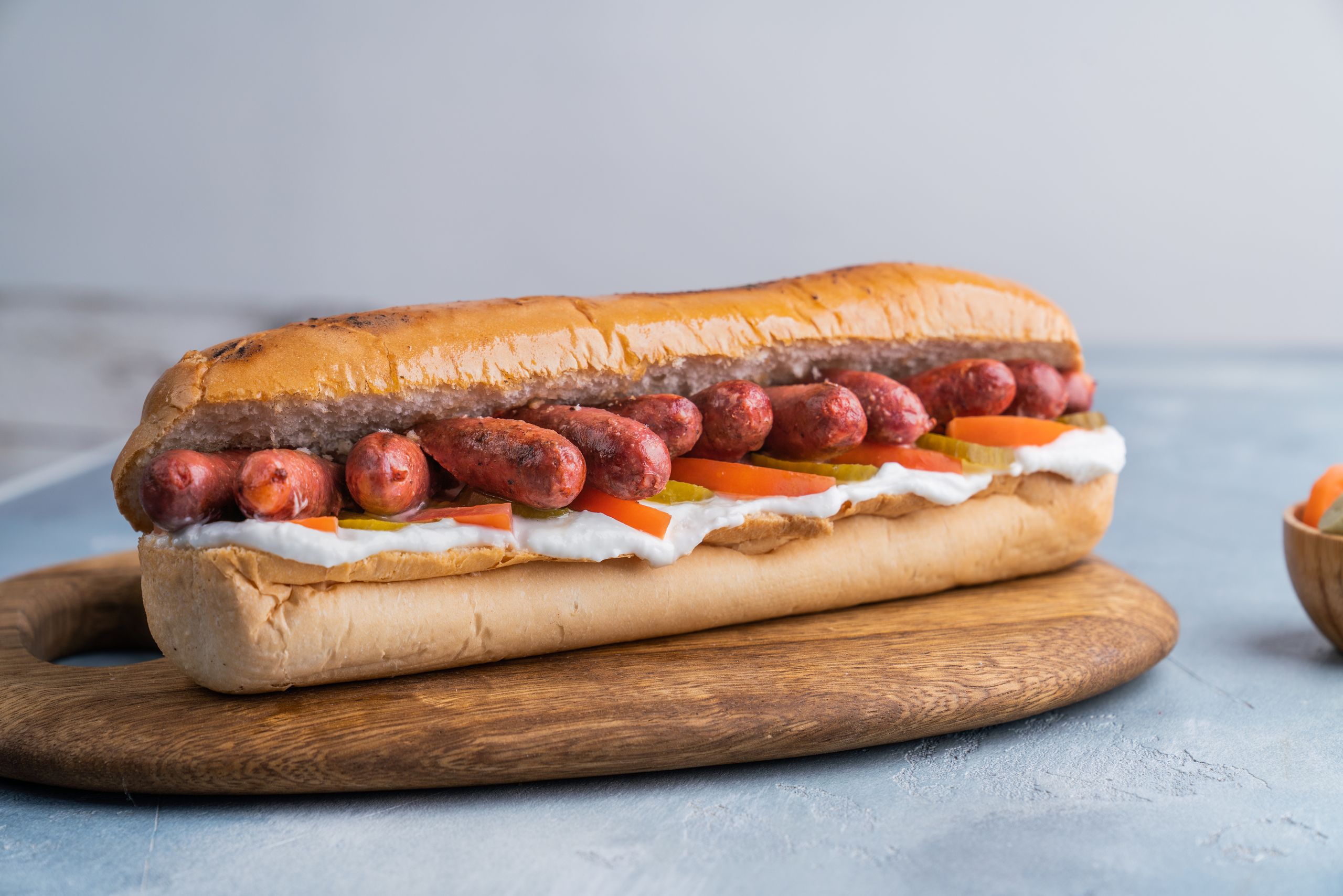 Deliciously presented hotdog with toppings on a wooden board, perfect for American food enthusiasts.