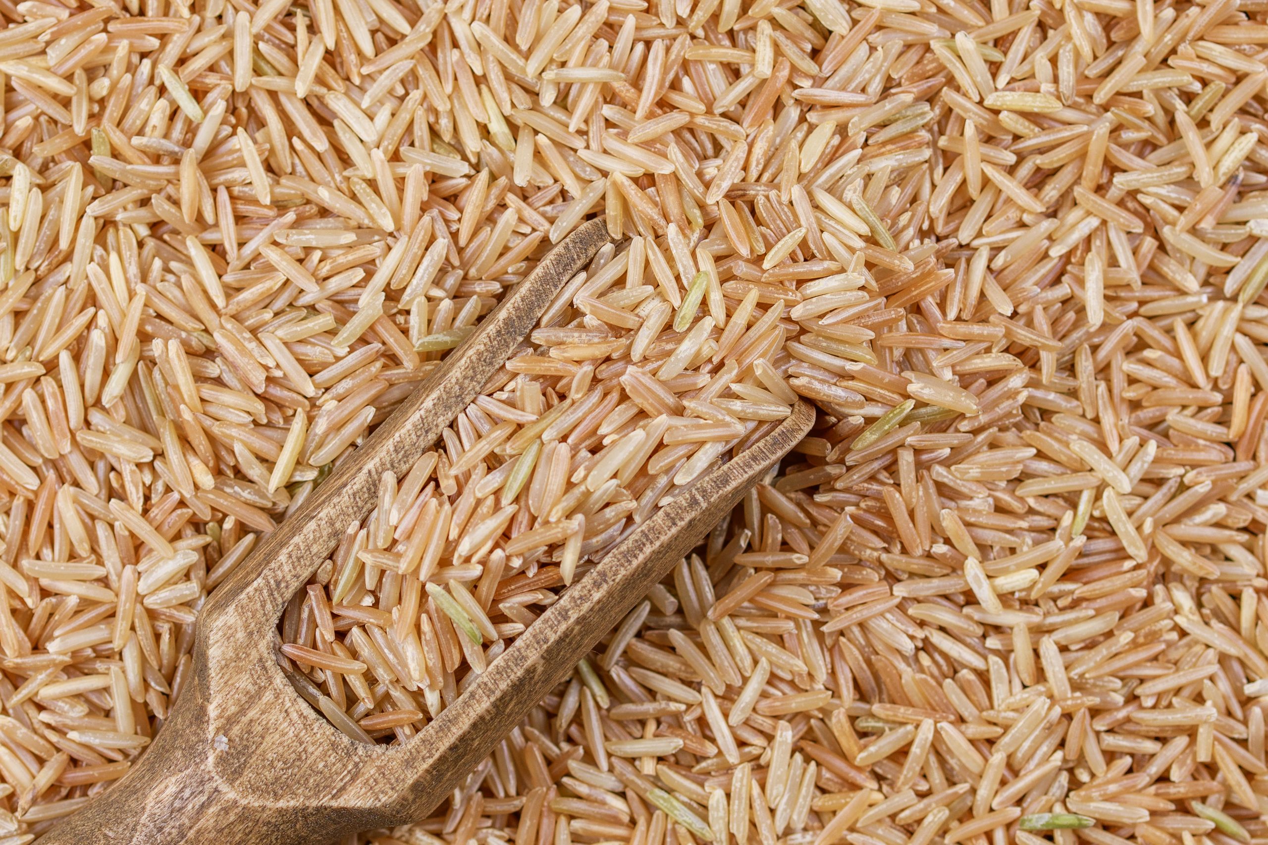 Detailed close-up of organic brown rice grains with a wooden scoop showcasing texture and natural colors.
