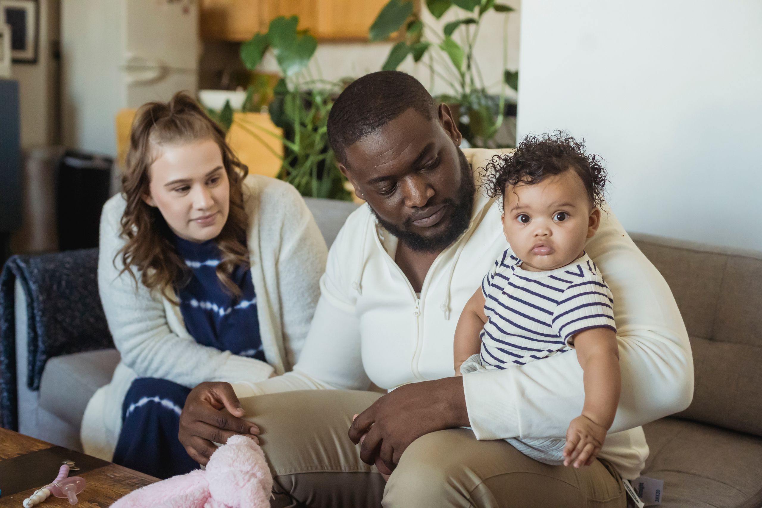 Diverse happy family with funny little adorable toddler on sofa in lounge in daytime