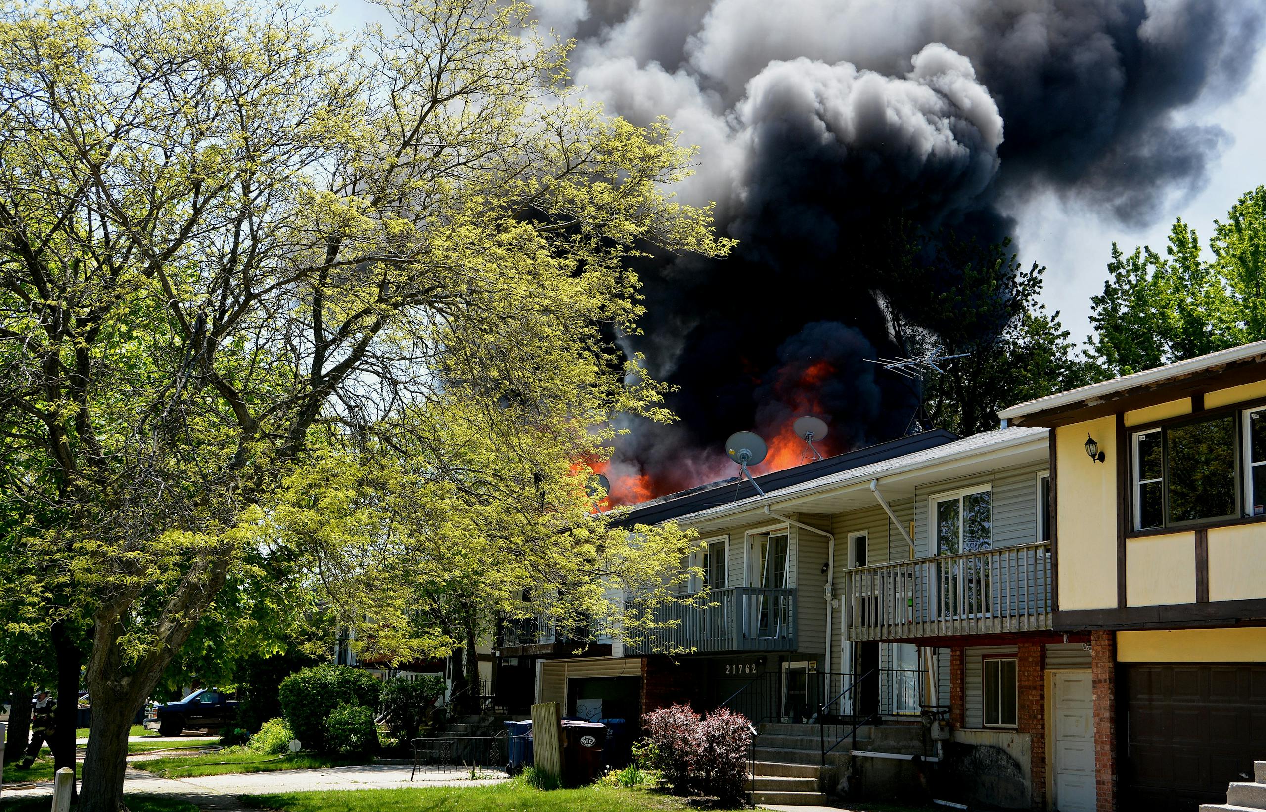 Dramatic house fire with thick smoke rising in a suburban neighborhood, surrounded by trees.