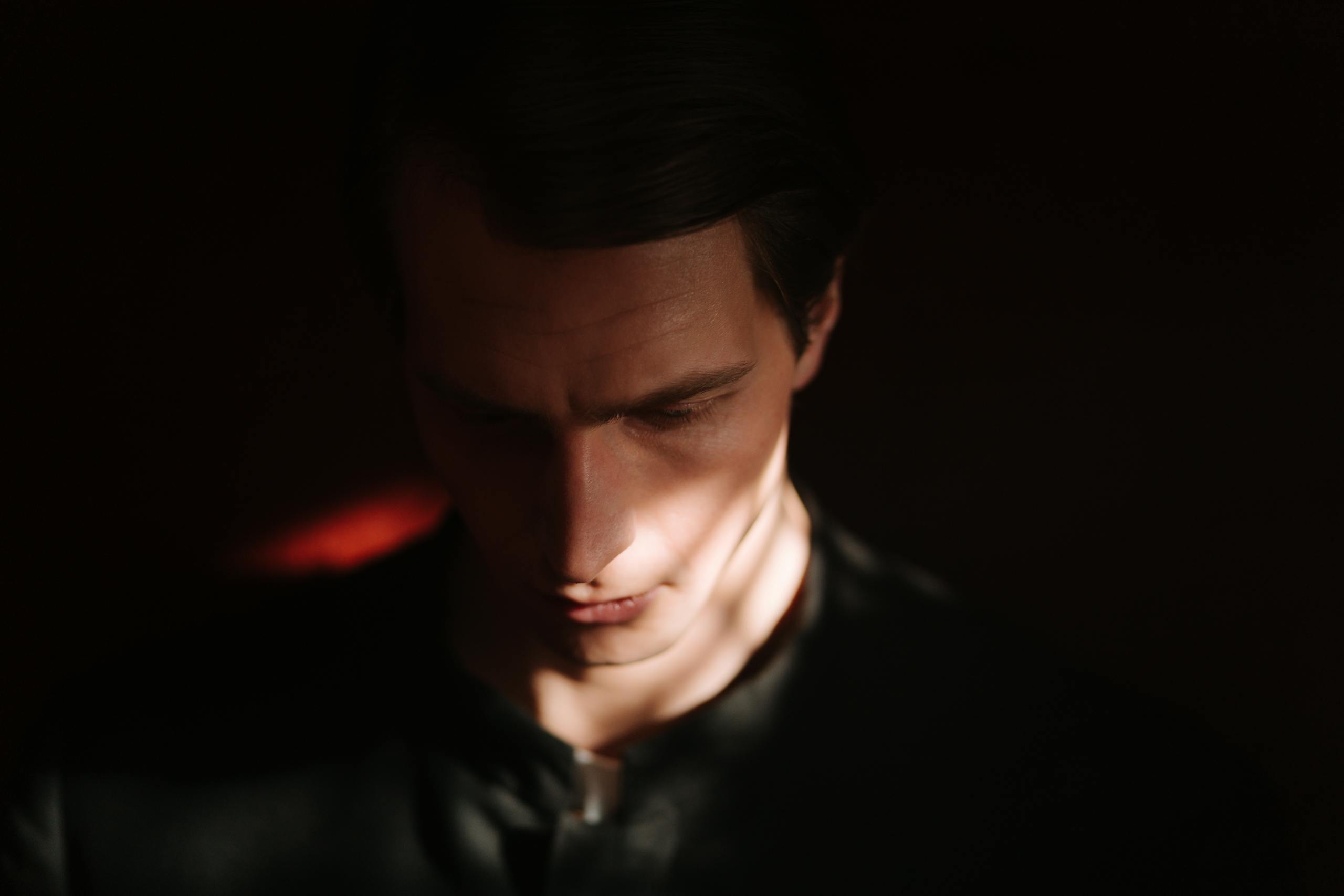 Dramatic low-light portrait of a man with soft shadows on face.