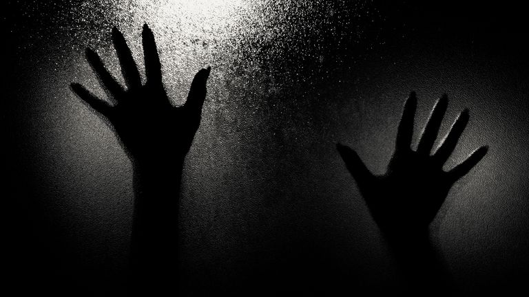 Dramatic silhouette of two hands pressed against a frosted glass, creating an eerie and mysterious ambiance.