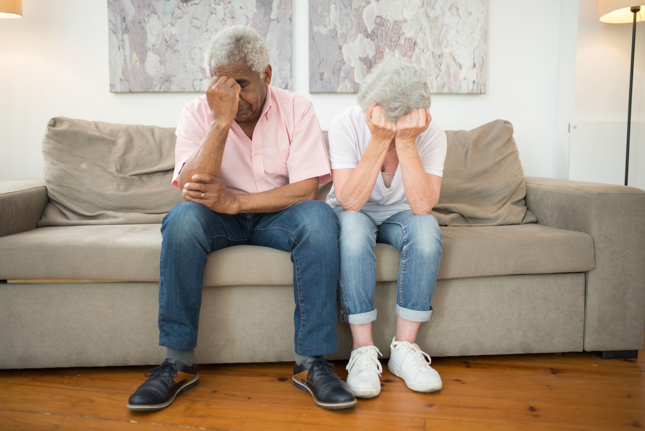 Elderly couple sitting on a sofa, showing emotions of sadness and grief at home.