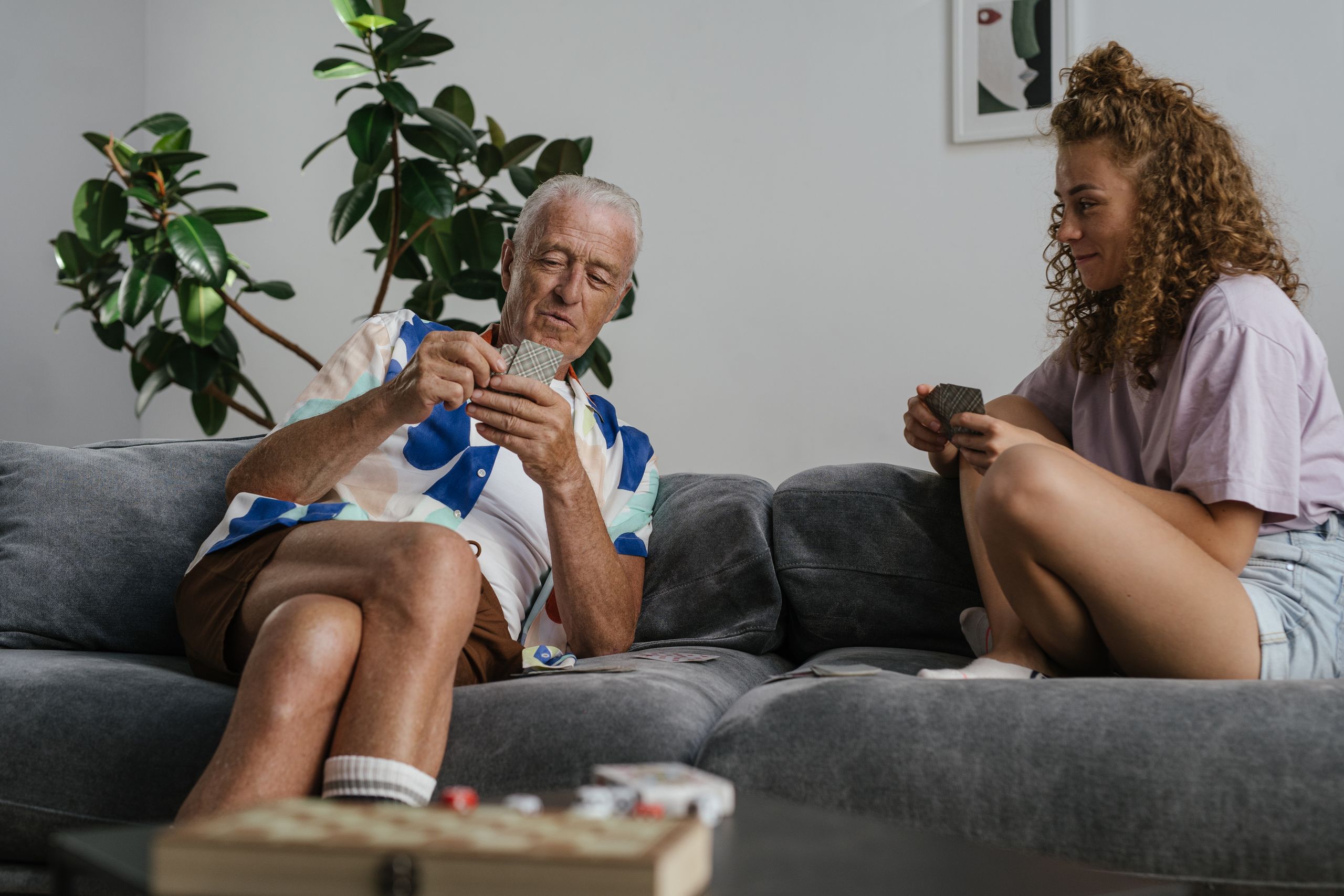 Elderly man and young woman playing cards on a couch, enjoying quality time together.