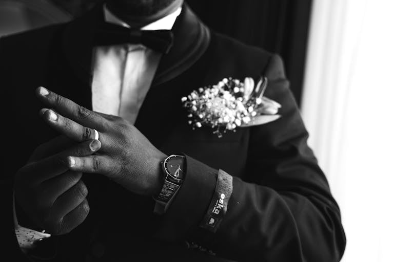 Elegant black and white portrait of a groom in formal attire showcasing a watch and wedding ring.