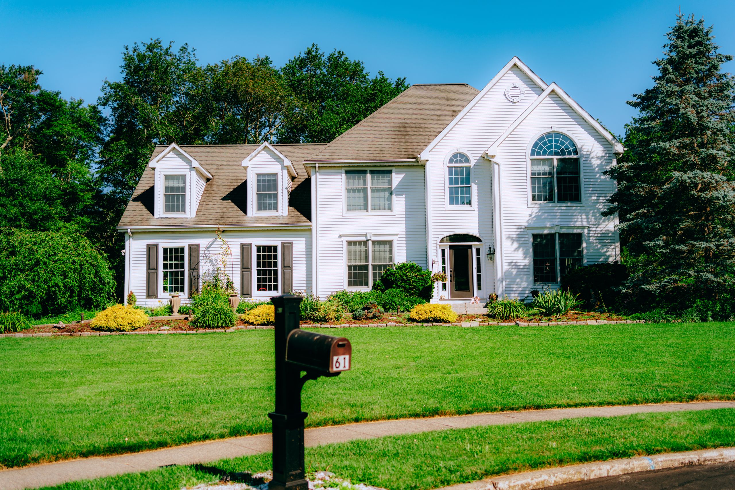 Elegant suburban house exterior with a lush green lawn and black mailbox featuring the number 61.
