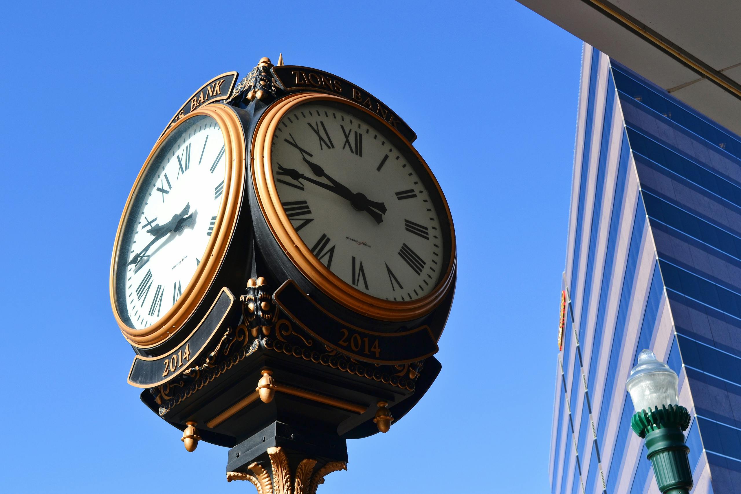 Elegant urban clock tower with Roman numerals against a clear blue sky and modern architecture.