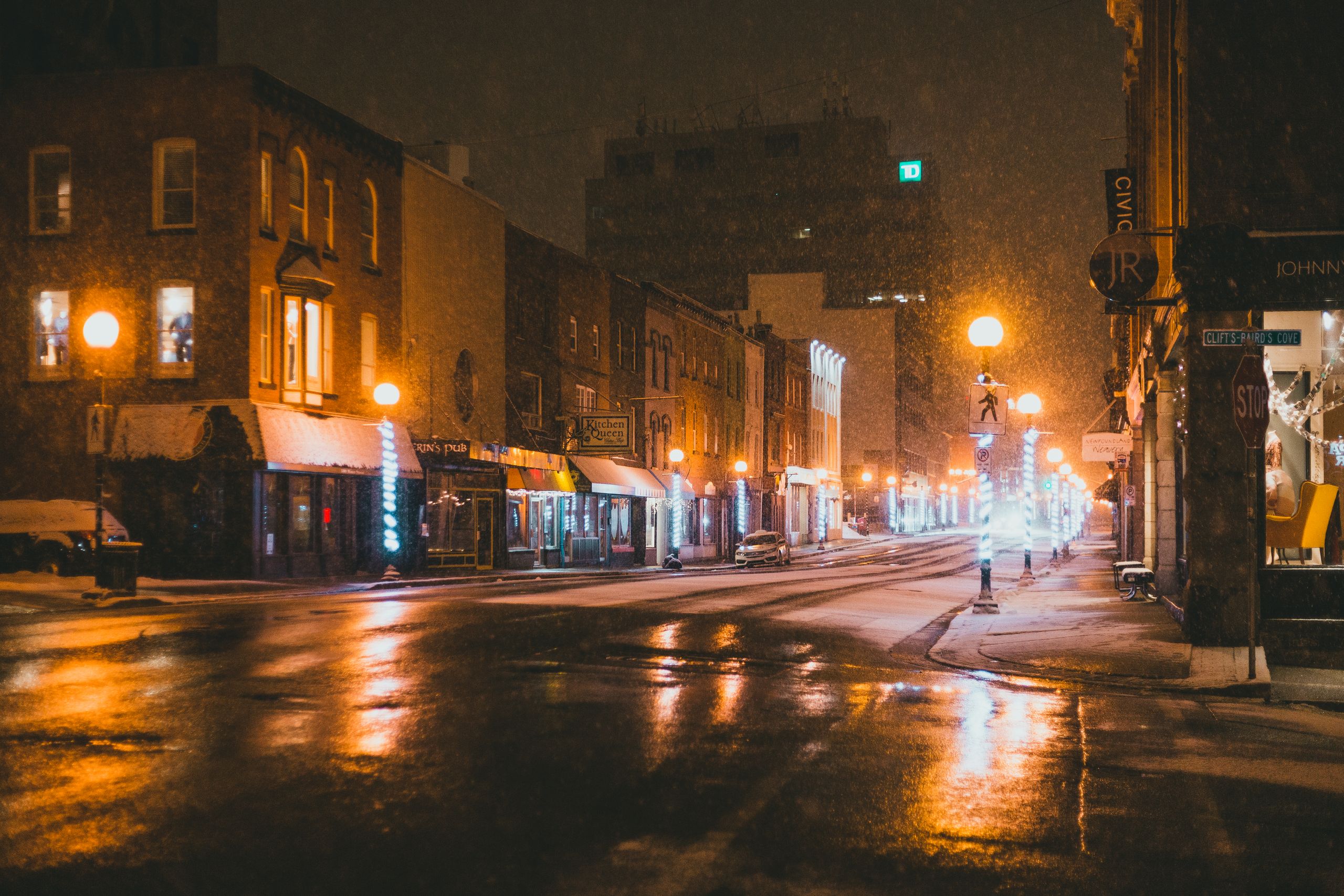Empty asphalt road between modern buildings with glowing lights and signboards on snowy night in winter