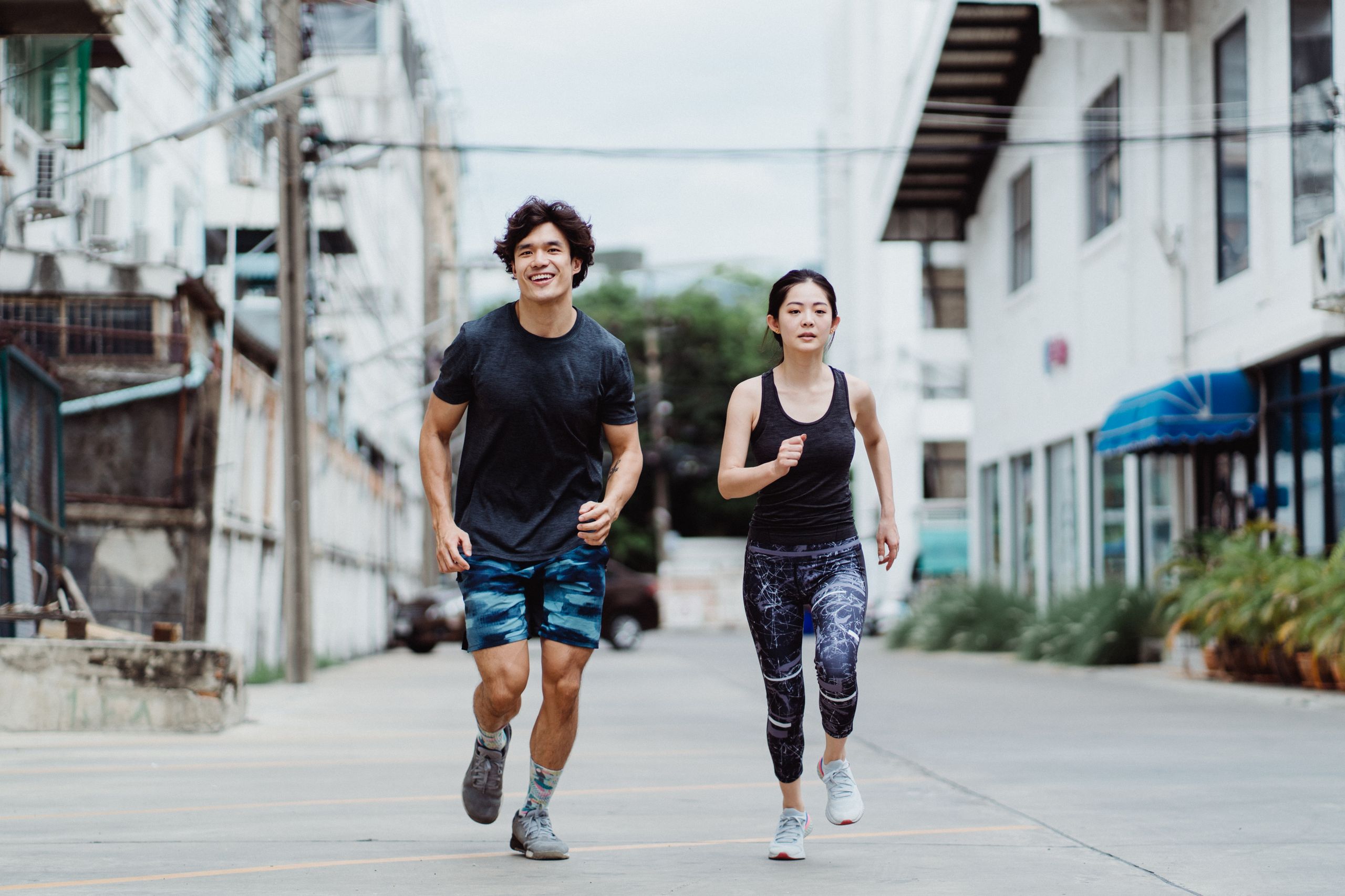 Energetic couple jogging outdoors in casual activewear in an urban environment, showcasing fitness and lifestyle.