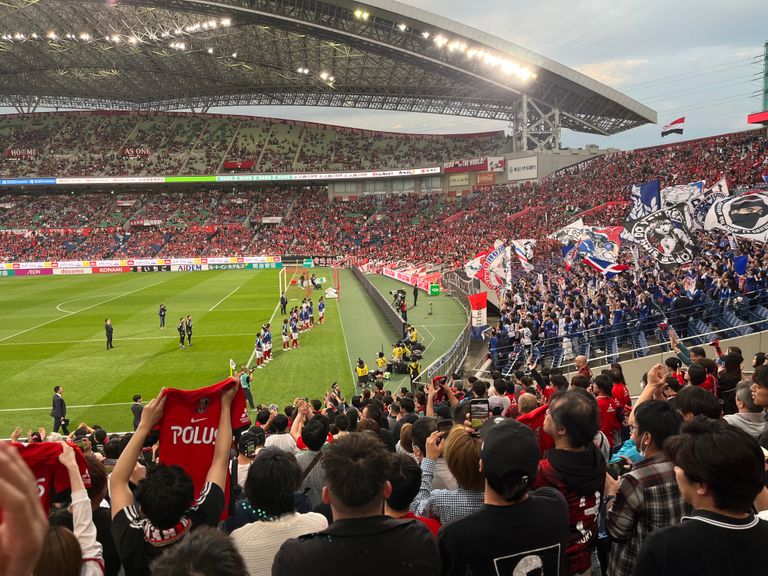 Energetic crowd cheering at a soccer match in Saitama Stadium, Japan.