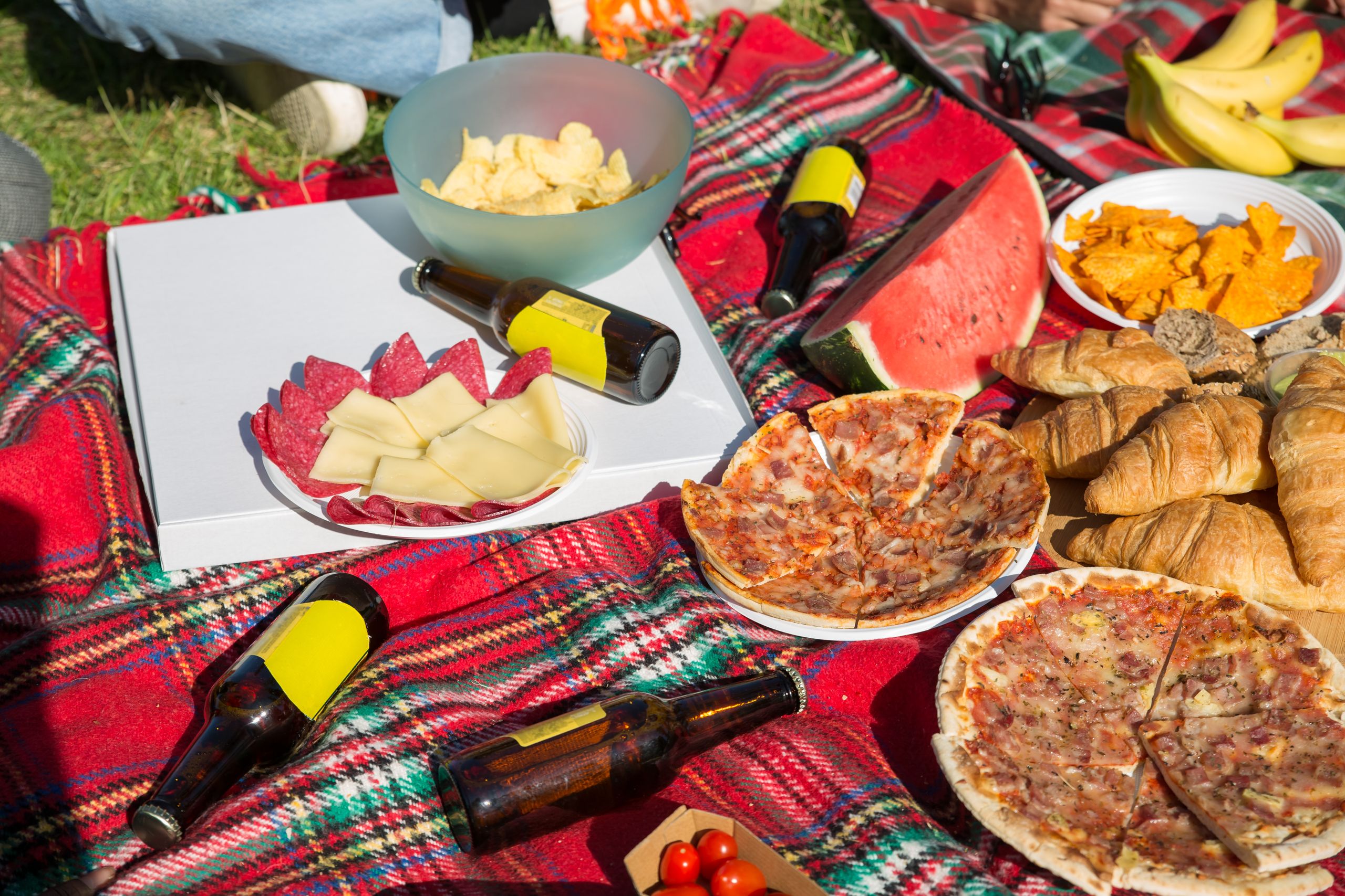 Enjoy a sunny picnic in Portugal with pizzas, snacks, and refreshing drinks on a lively plaid blanket.