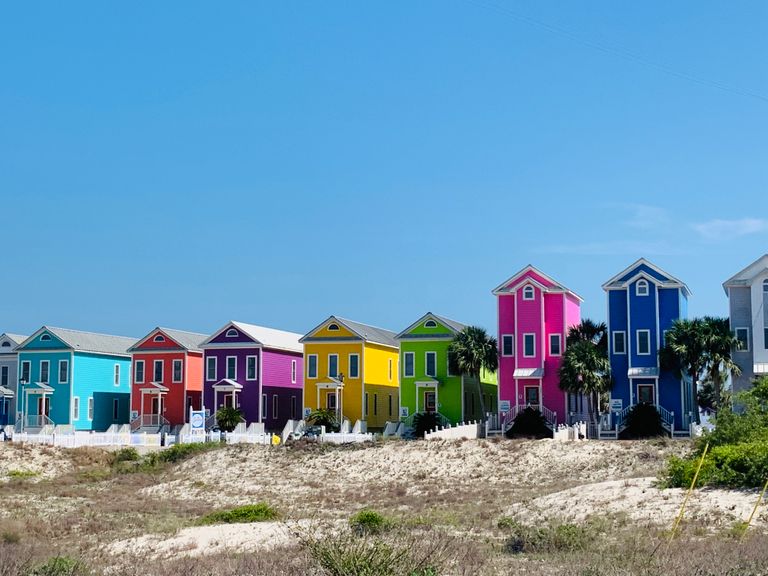Exterior of colorful residential townhouses located on hilly terrain with random greenery under clear blue sky