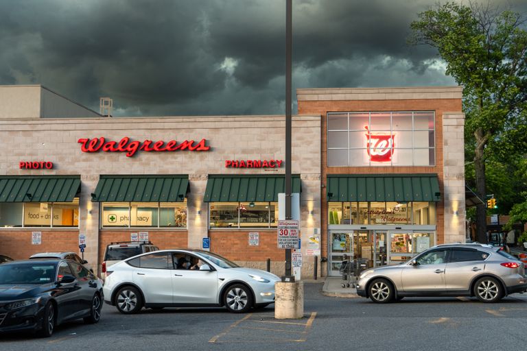 Exterior view of a Walgreens pharmacy under dark storm clouds with cars in the parking lot.