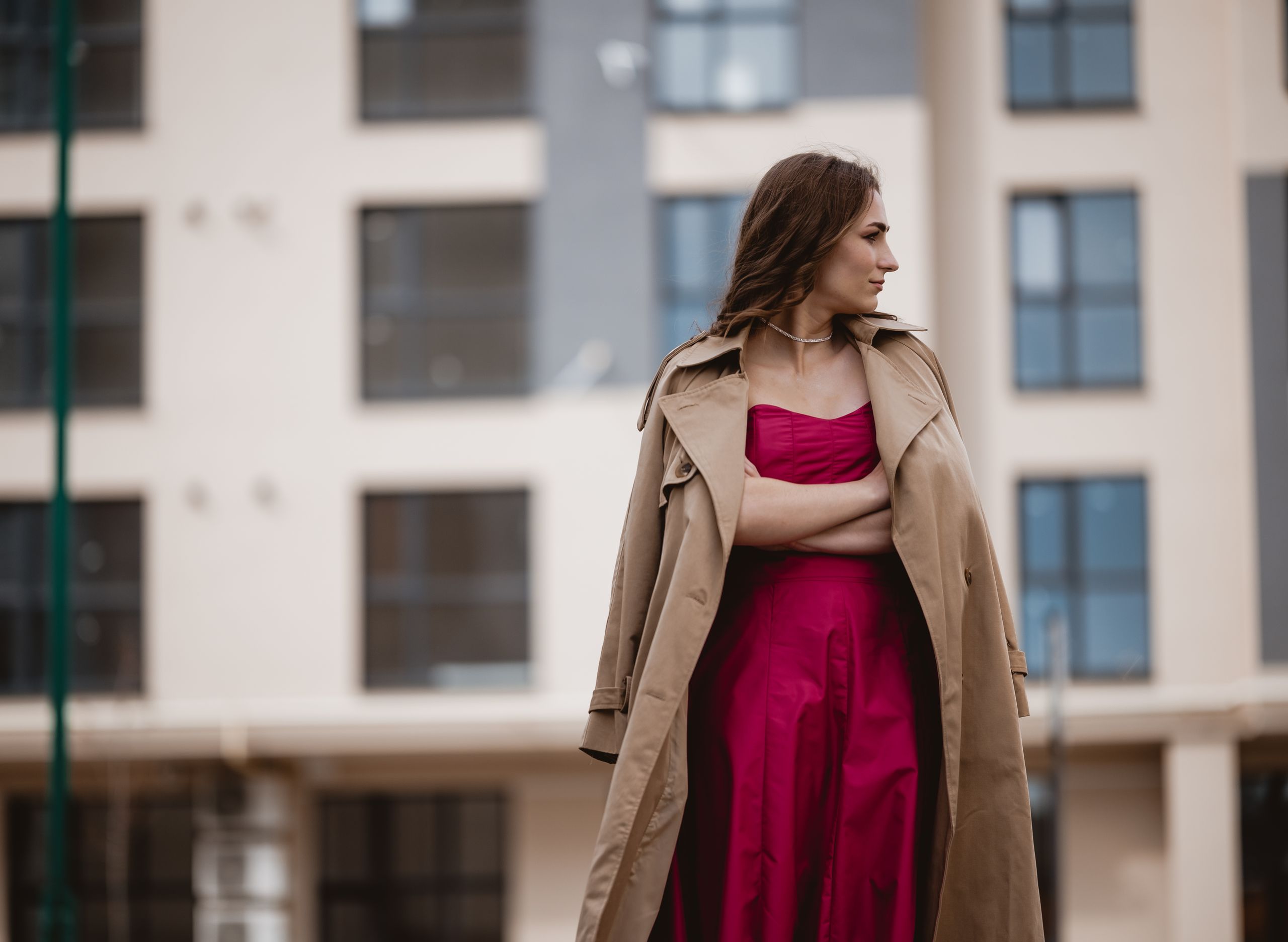Fashionable woman wearing a pink gown with a trench coat, posing in front of an office building.