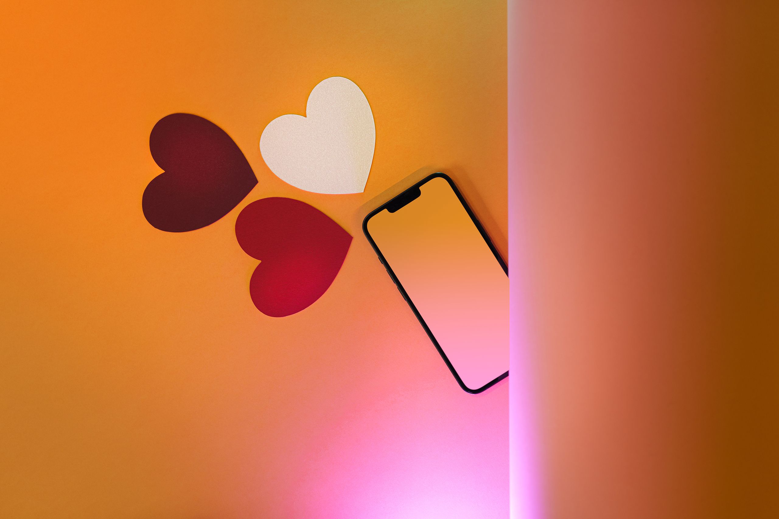 Flat lay of paper hearts and smartphone on orange background, perfect for Valentine's themes.