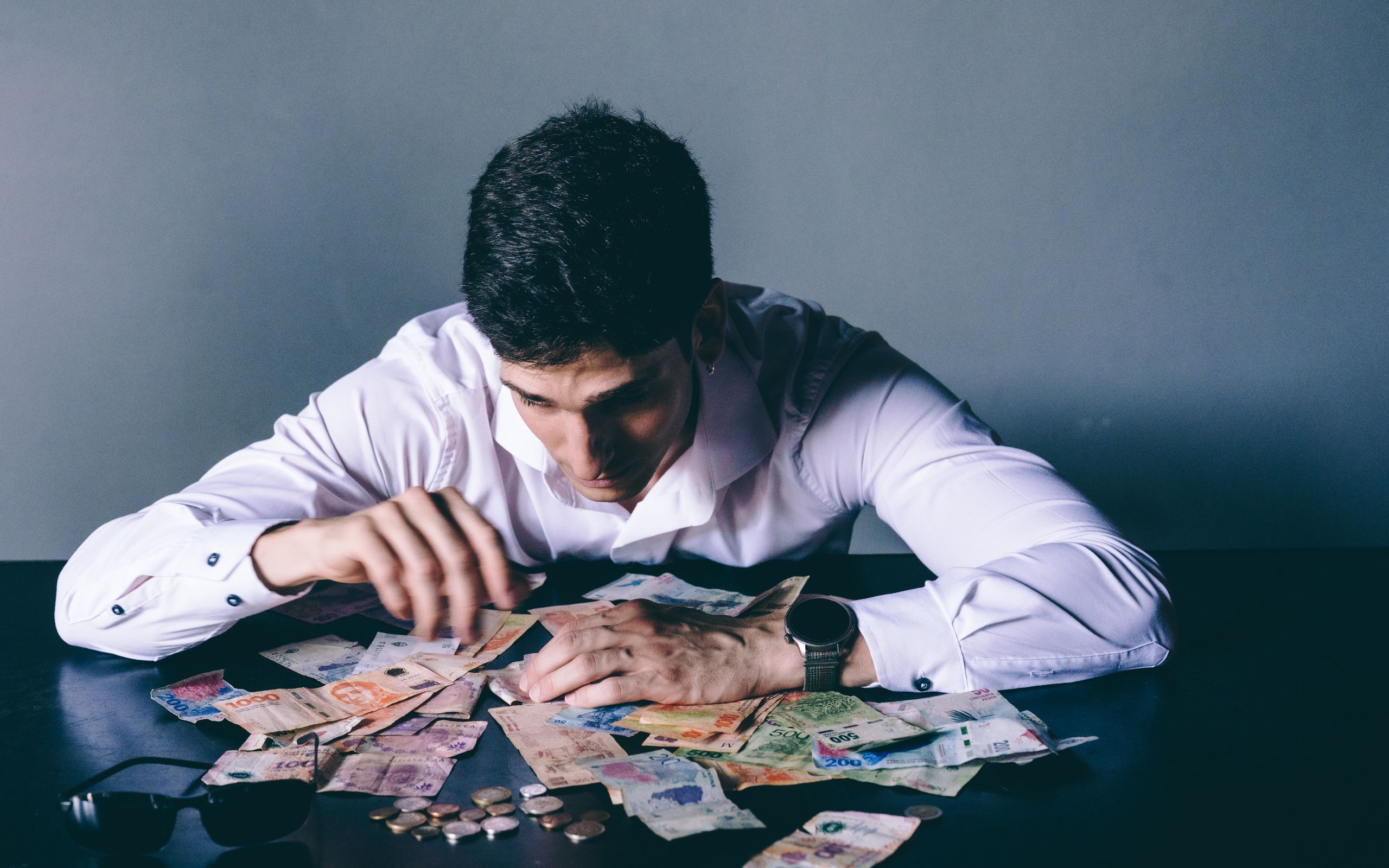 Focused man counts various international currencies on a dark desk indoors.