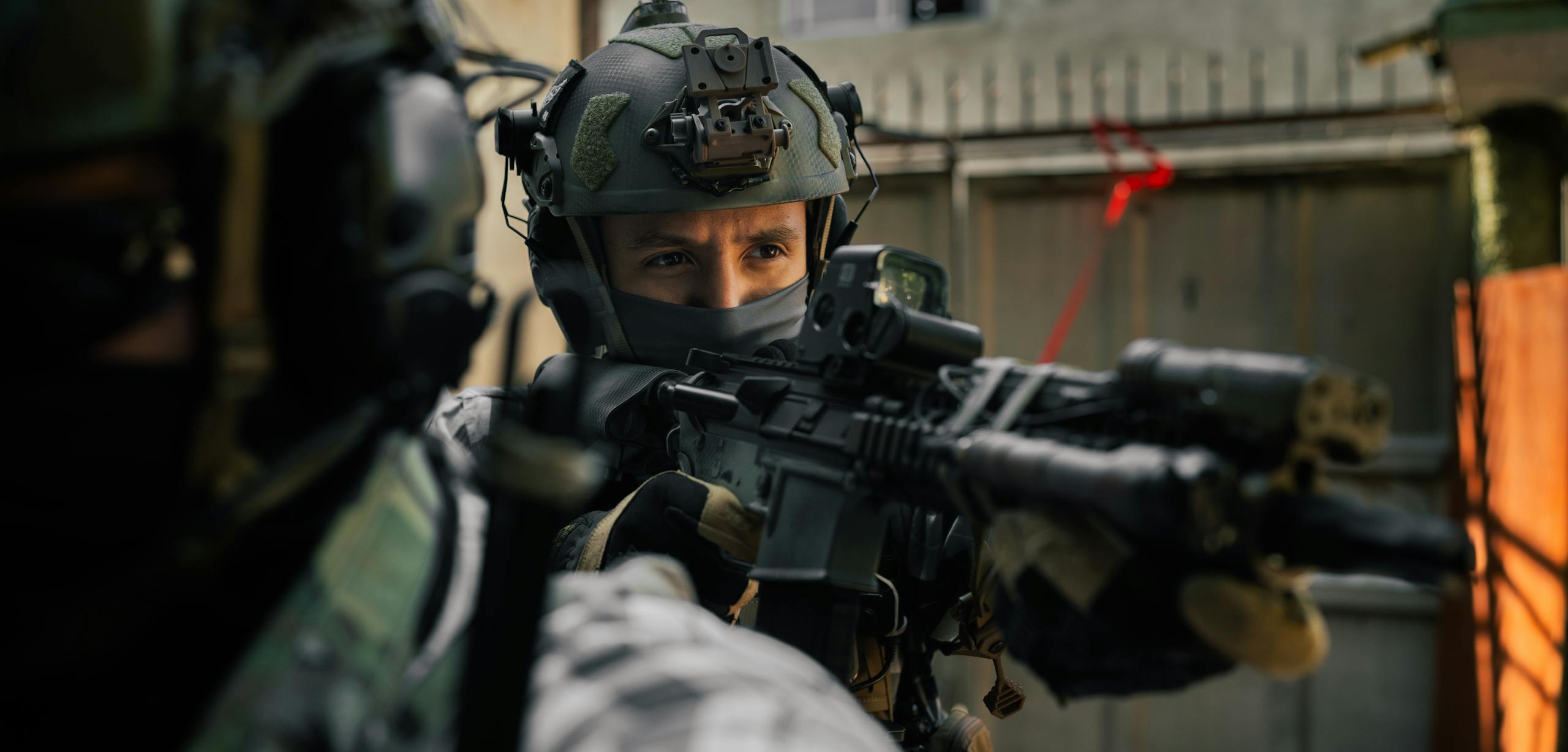 Focused soldier in tactical gear aiming rifle during an outdoor operation.