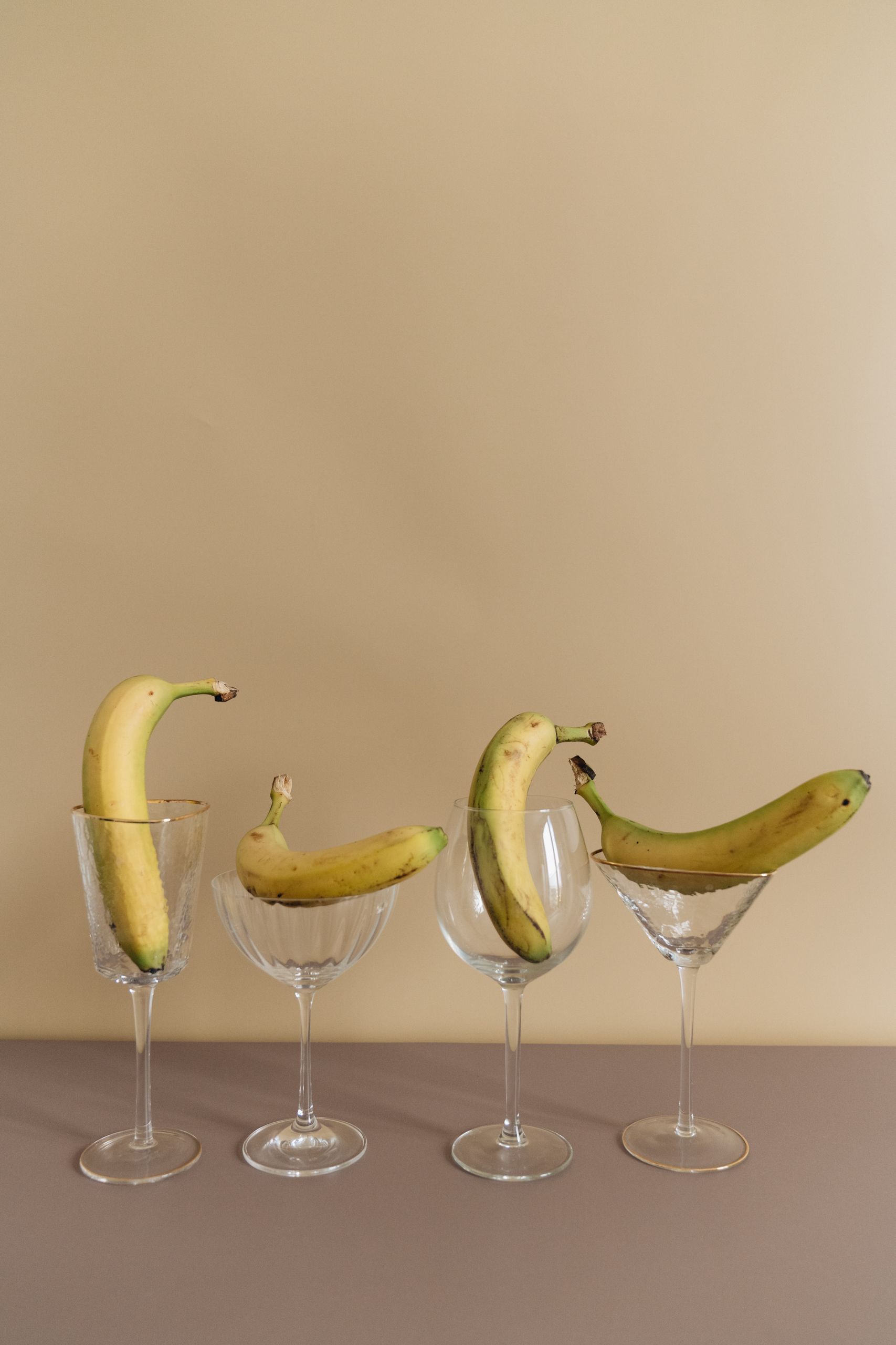 Four bananas creatively positioned in elegant wine glasses, showcasing minimalist food art.