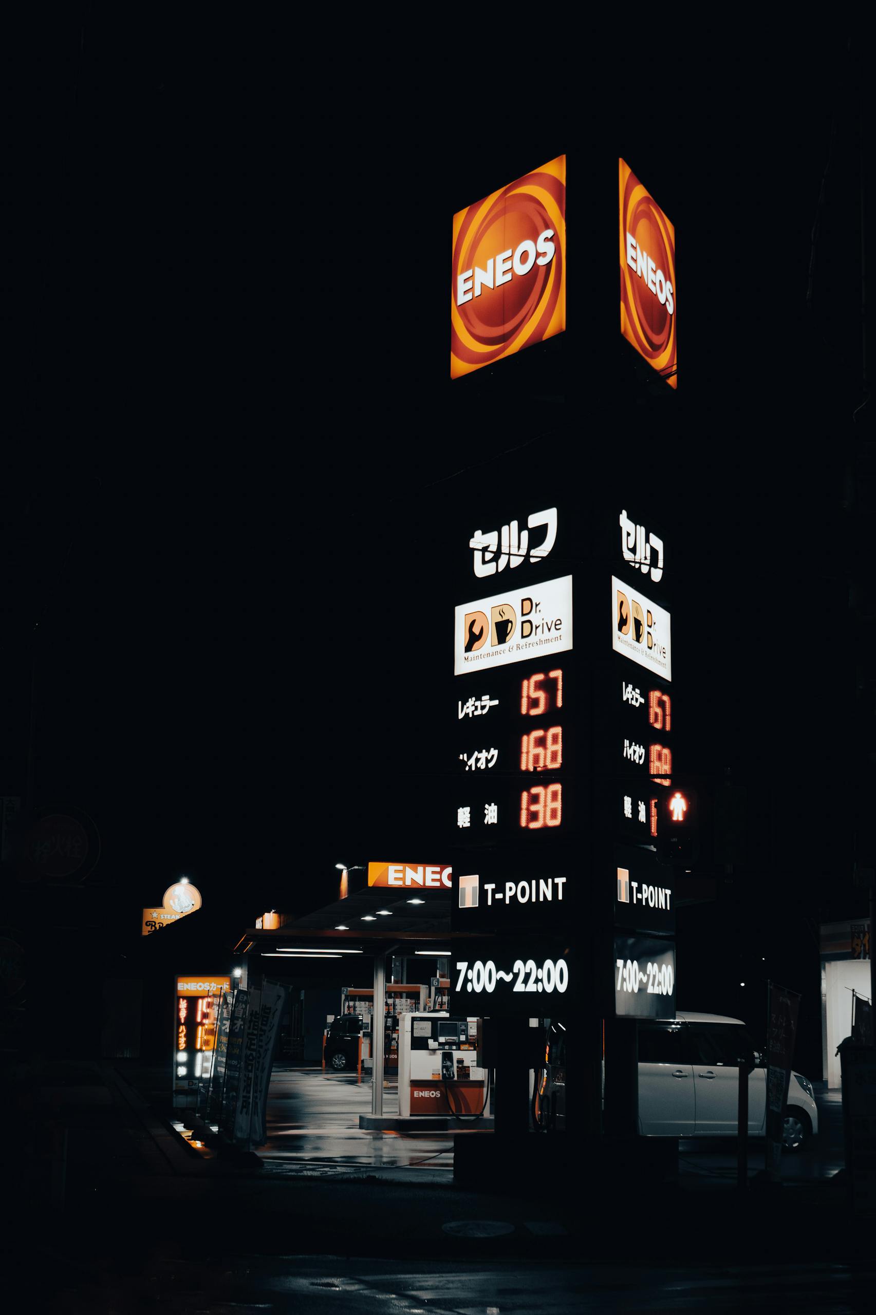 Framed shot of a lit ENEOS gas station in Toyohashi, Japan at night, showcasing fuel prices and signs.