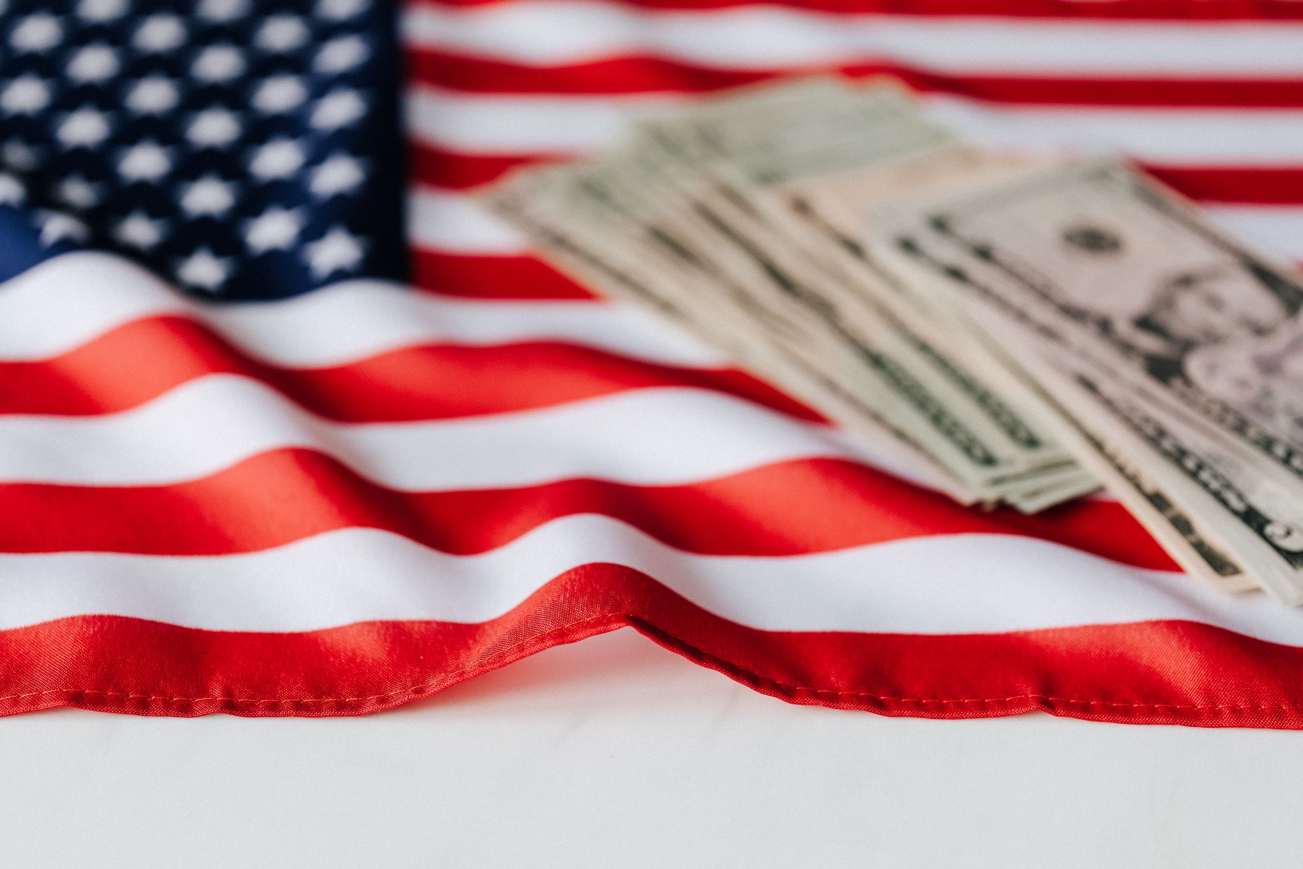 From above of American dollars heap placed on colorful national flag on white surface