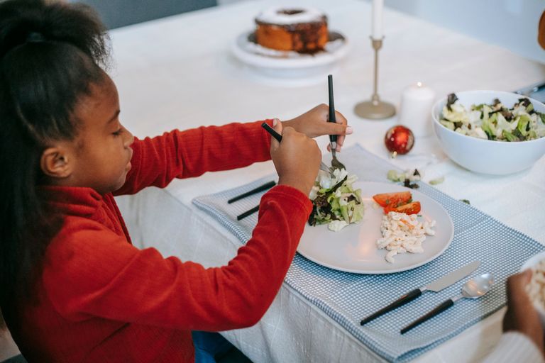 From above, a side view of African American preteen child putting salad on plate while sitting at table during holiday dinner