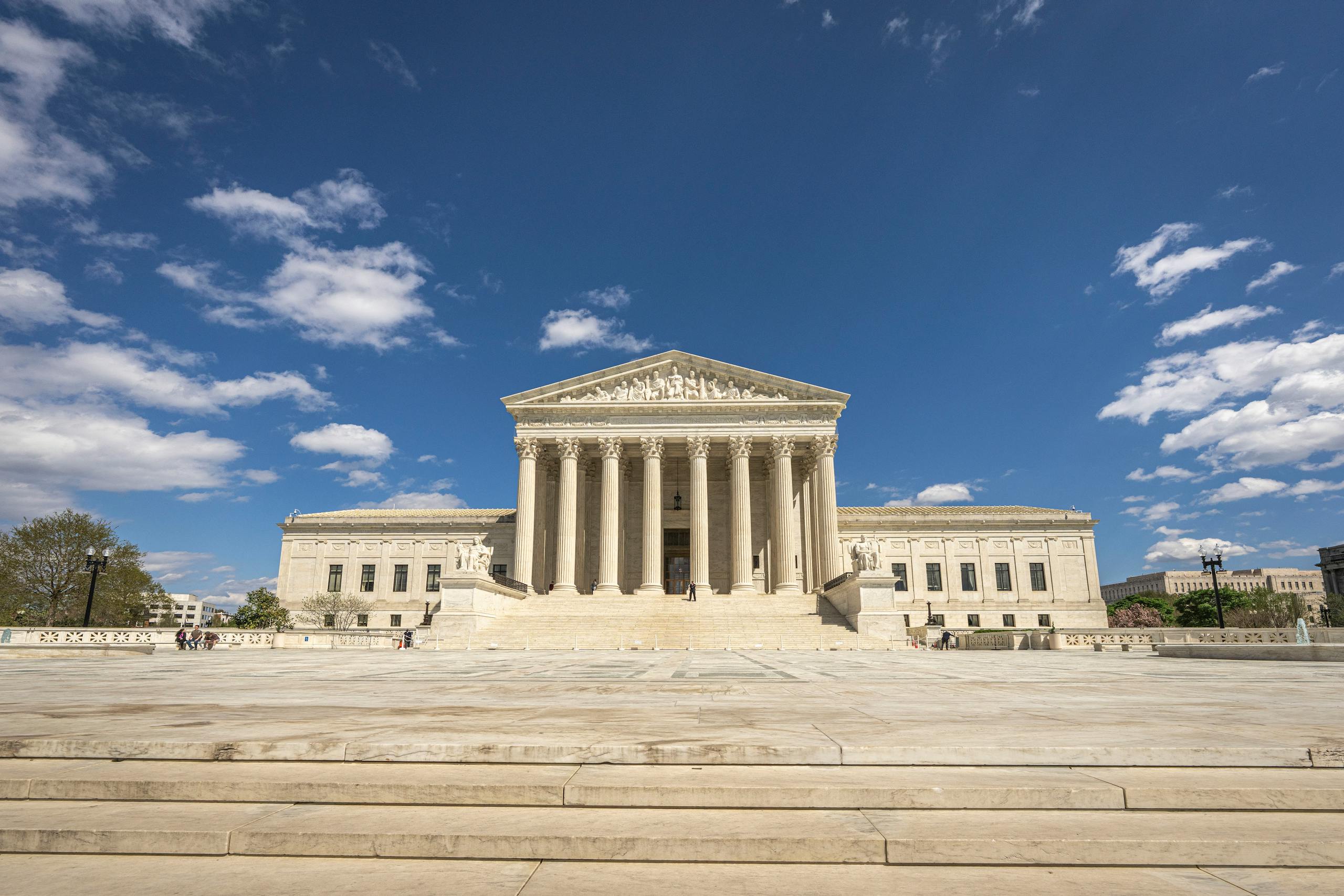 Front view of the United States Supreme Court building on a sunny day with blue sky and clouds.
