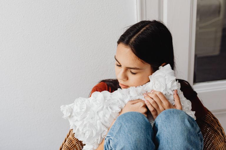 Girl with closed eyes holding a white rose-like pillow, expressing comfort and peace indoors.