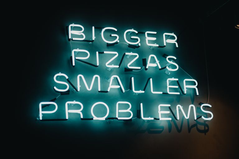 Glowing neon sign with humorous message about pizza in a São Paulo restaurant.