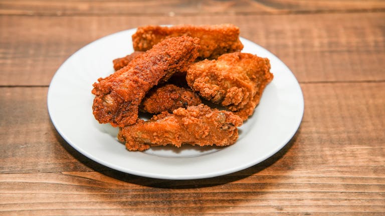 Golden brown crispy fried chicken wings served on a white plate, perfect for a tasty meal or snack.