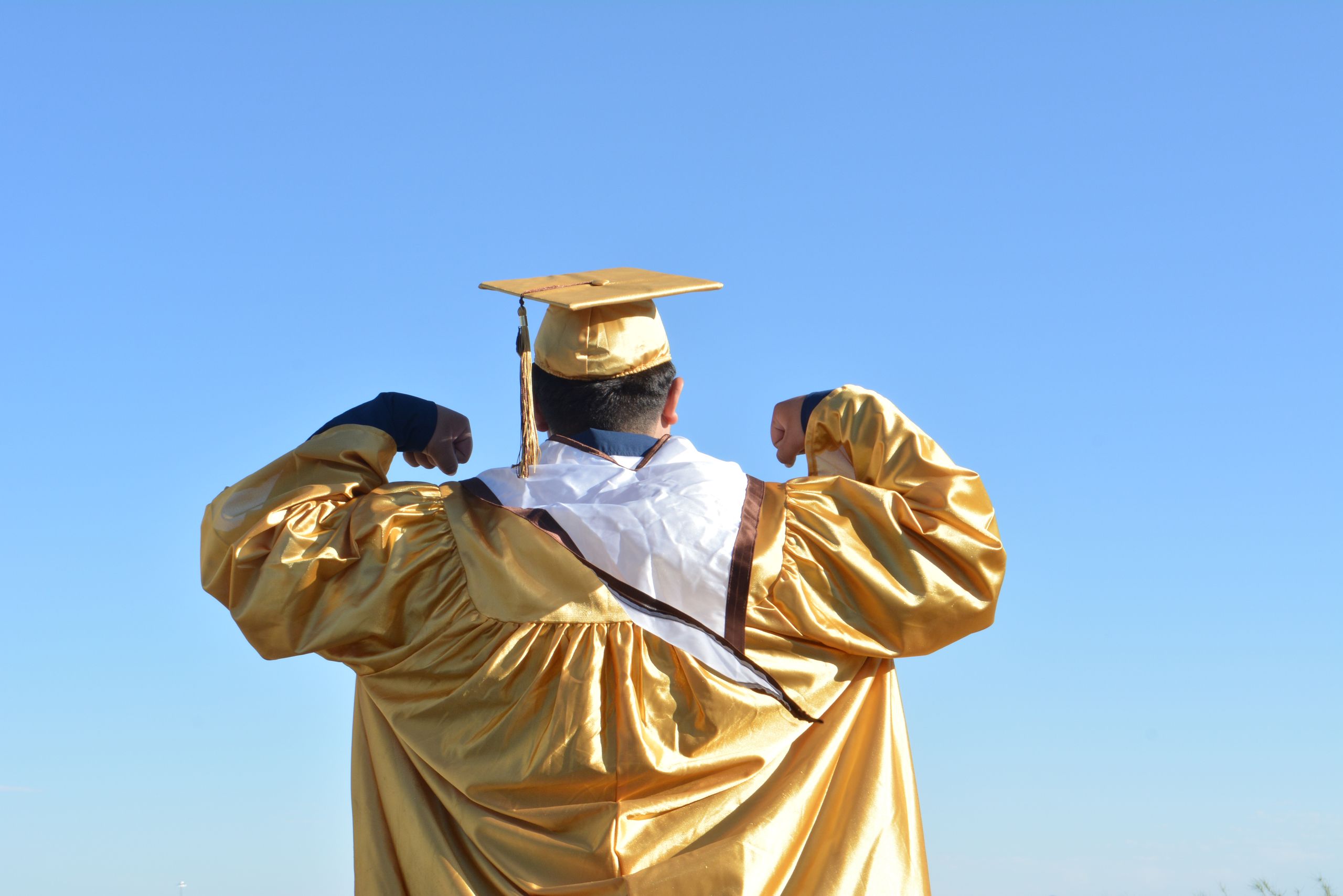 Graduating in style with a gold gown against a clear blue sky, celebrating achievement and new beginnings.