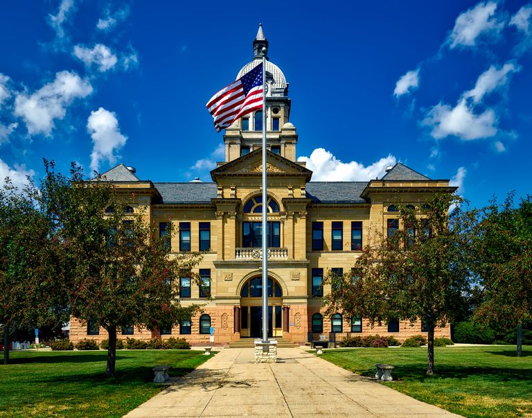 Grand courthouse in Cedar Rapids with an American flag in a bright blue sky.