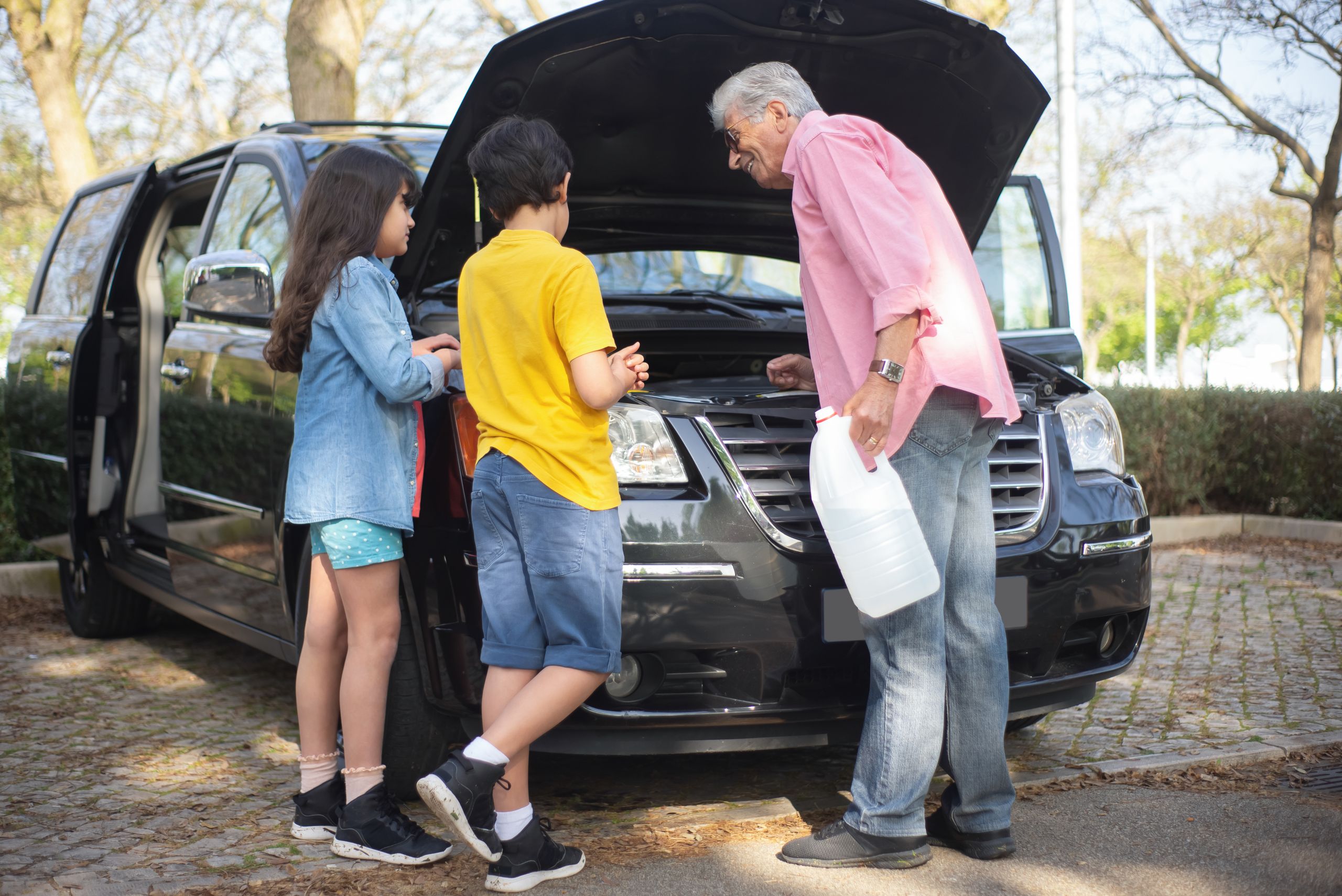 Grandfather and grandchildren are checking car engine outdoors in Portugal.