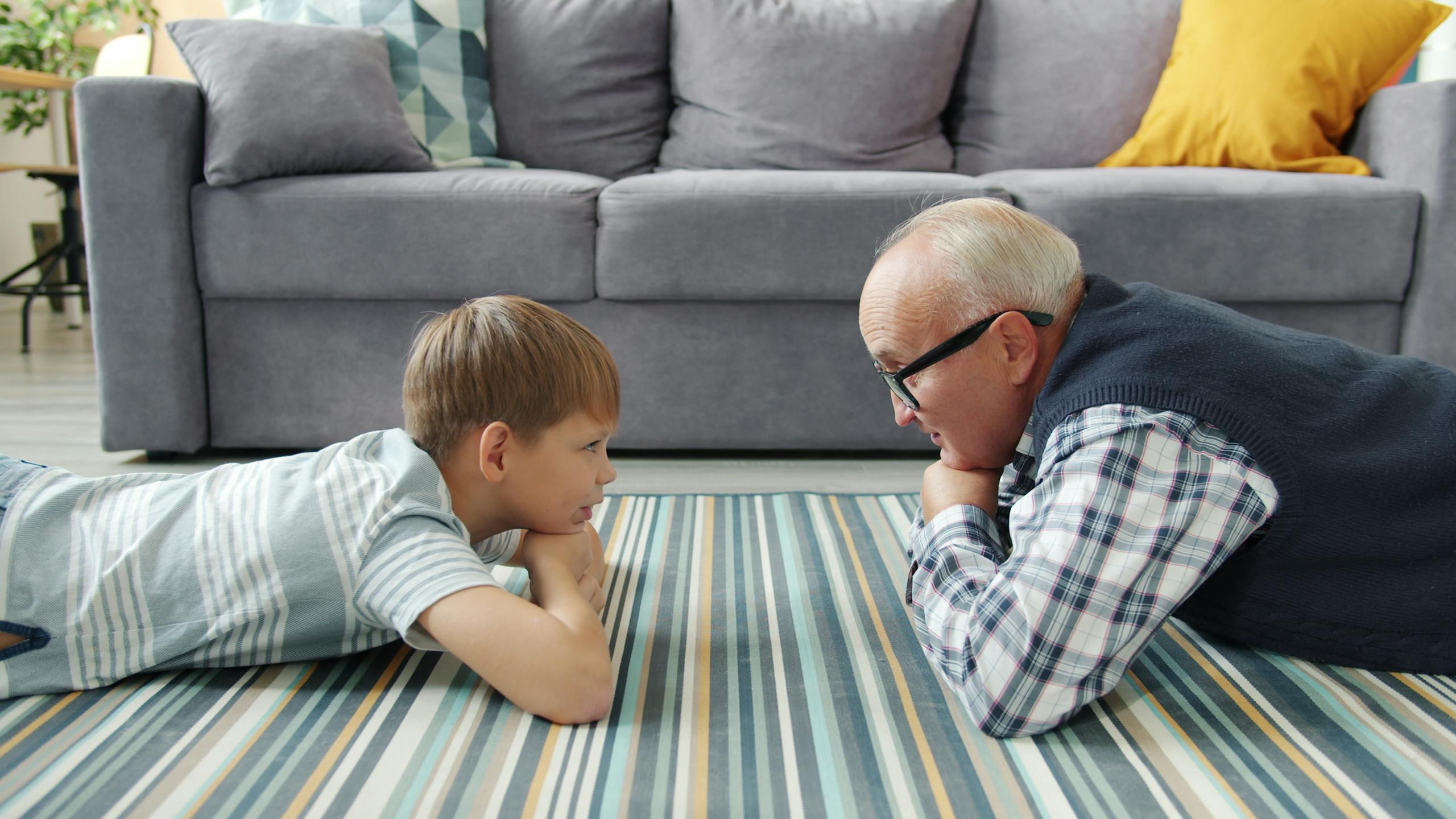 Grandfather and grandson enjoying quality time together at home, lying on floor.