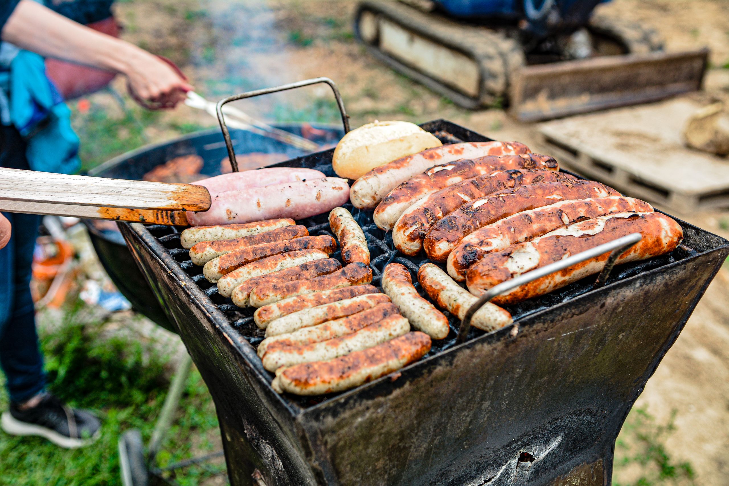 Grilling an assortment of sausages and bread at an outdoor barbecue on a sunny day.